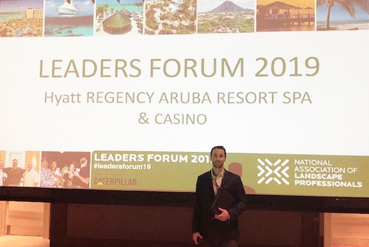 Drew Garcia standing in front of the giant Leaders Forum 2019 screen