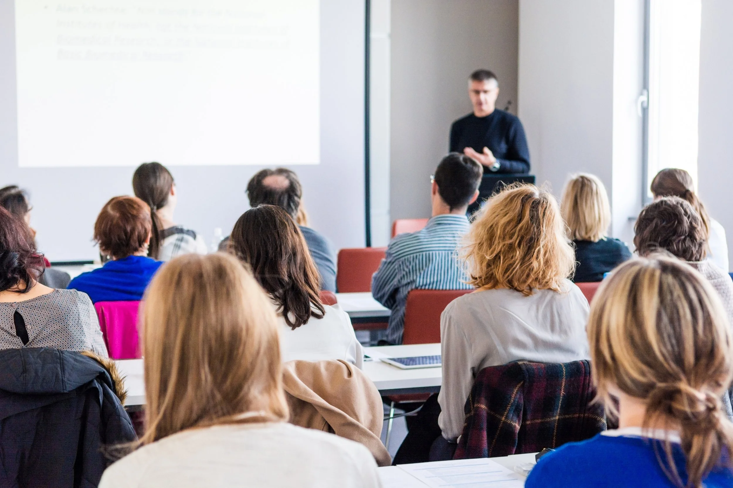 Classroom of adults with a male speaker at the front of the room.