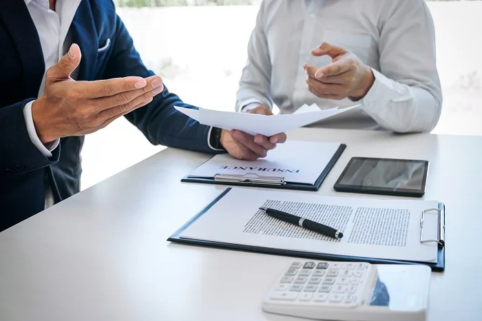 Two men holding insurance papers and discussing them at a table