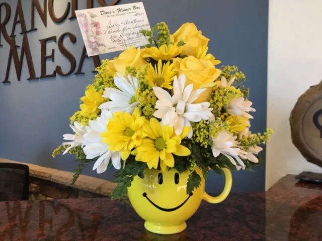 Bouquet of yellow and white flowers in a smiley face yellow vase.