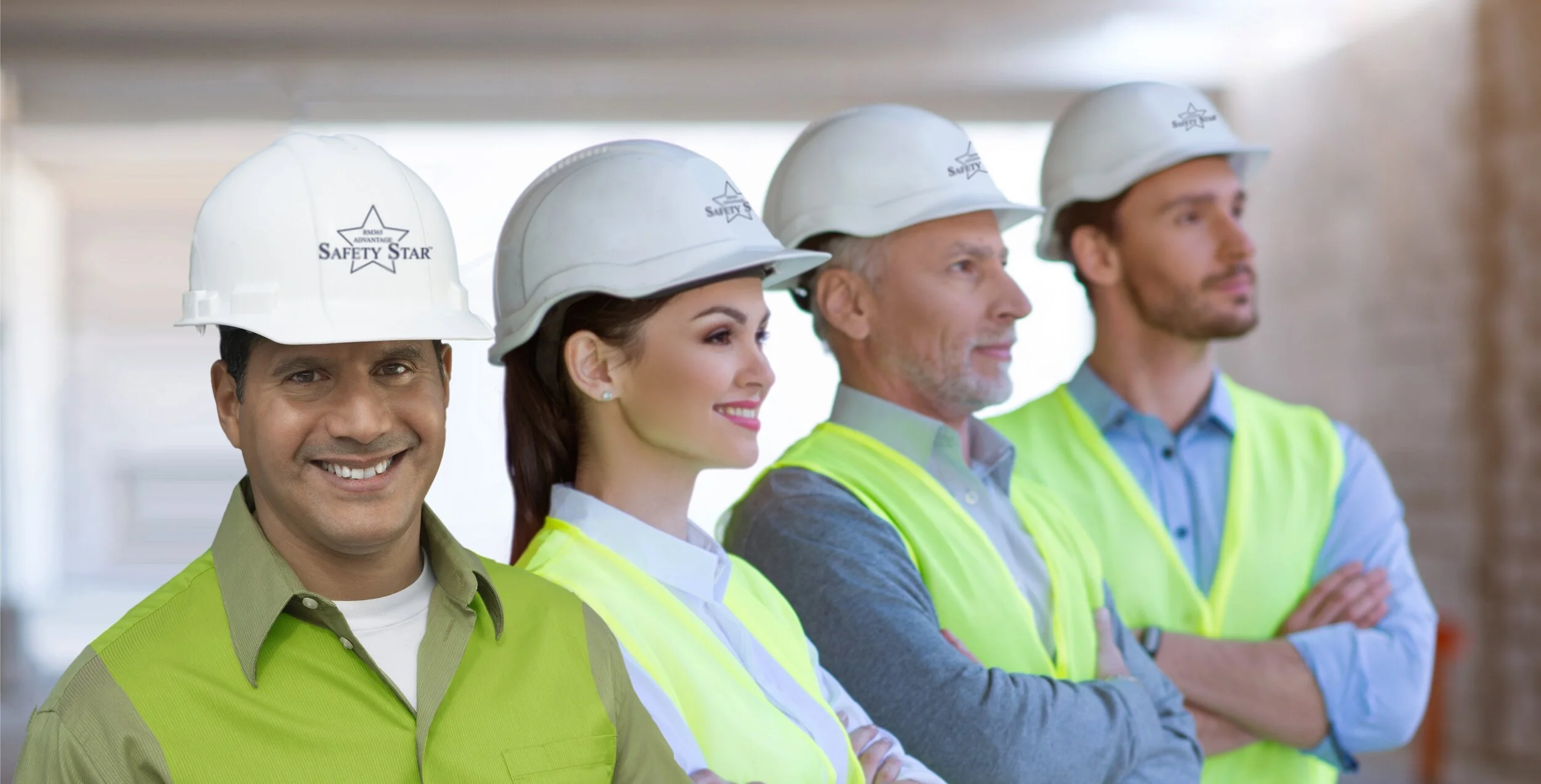 Group of four construction professionals wearing white safety helmets and high-visibility vests, standing in a row indoors.