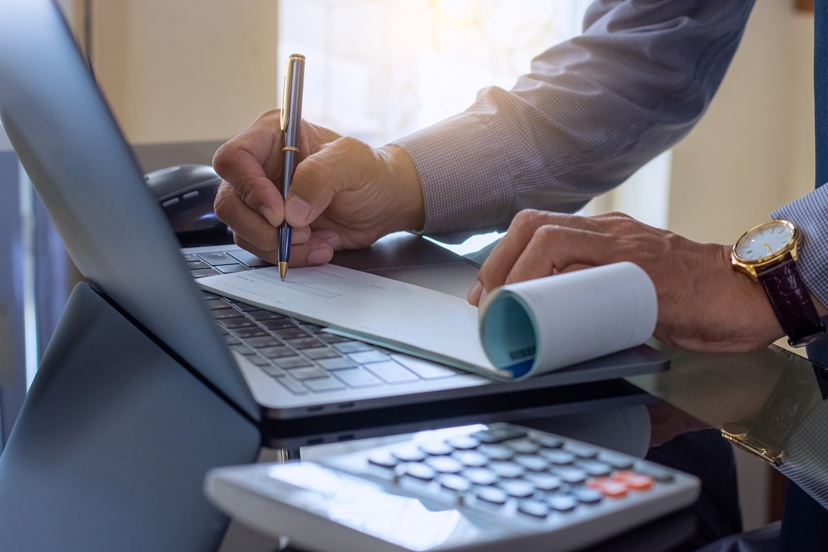 Business man hand writing and signing cheque book with laptop computer on the wooden table at modern home office (1200).jpg
