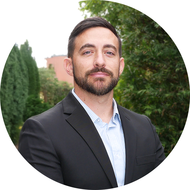 Kyle Dunlap, a dark -haired male with beard wearing a dark suite and light blue button up shirt.