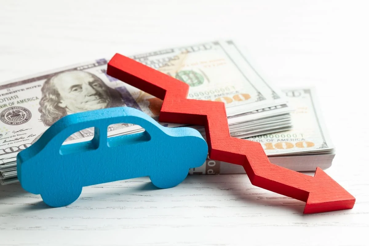 Wooden car, stack of money, and red arrow pointing down.jpg