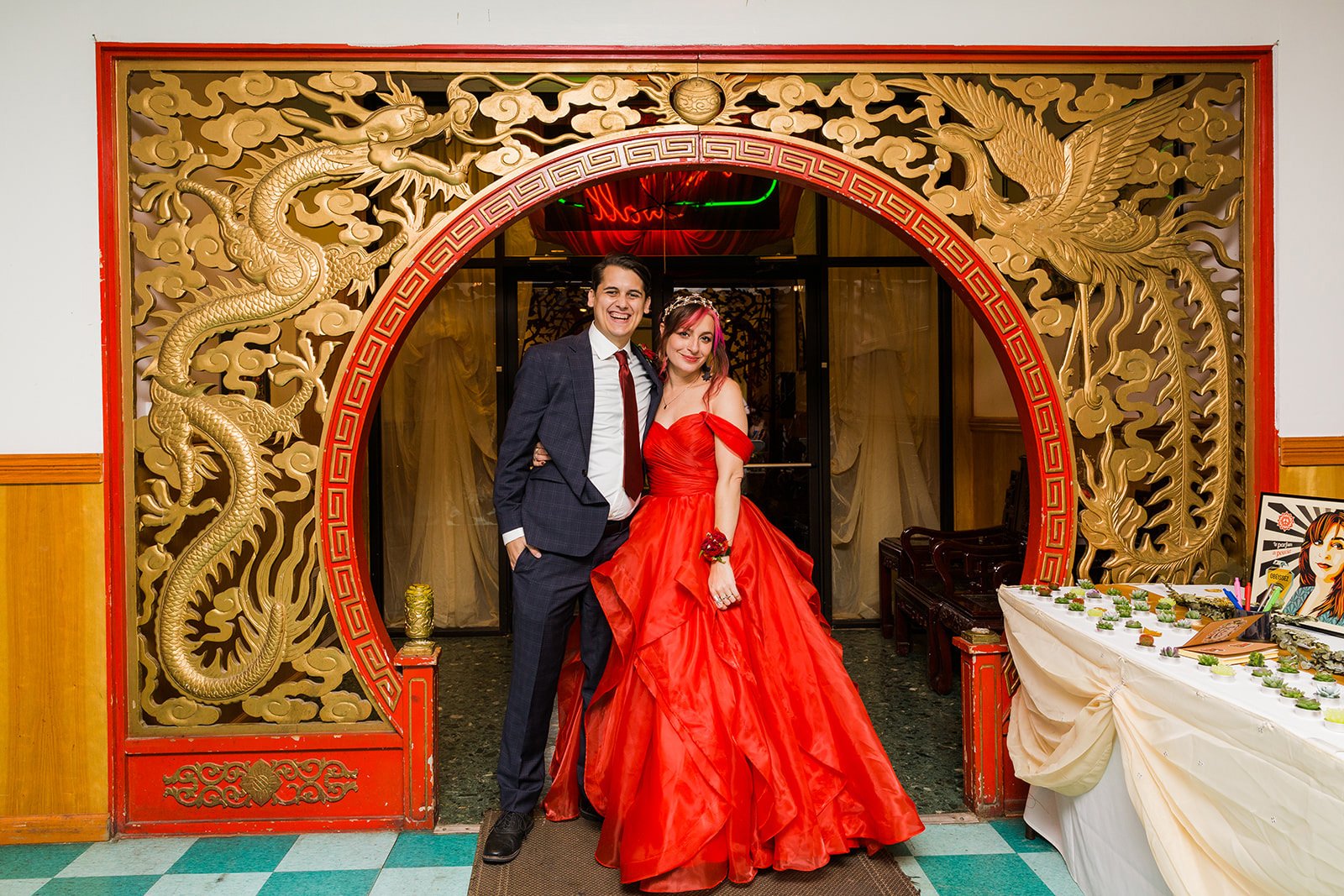  Bride in nontraditional red wedding dress poses with groom under decorative arch at dim sum restaurant Furama in Chicago 