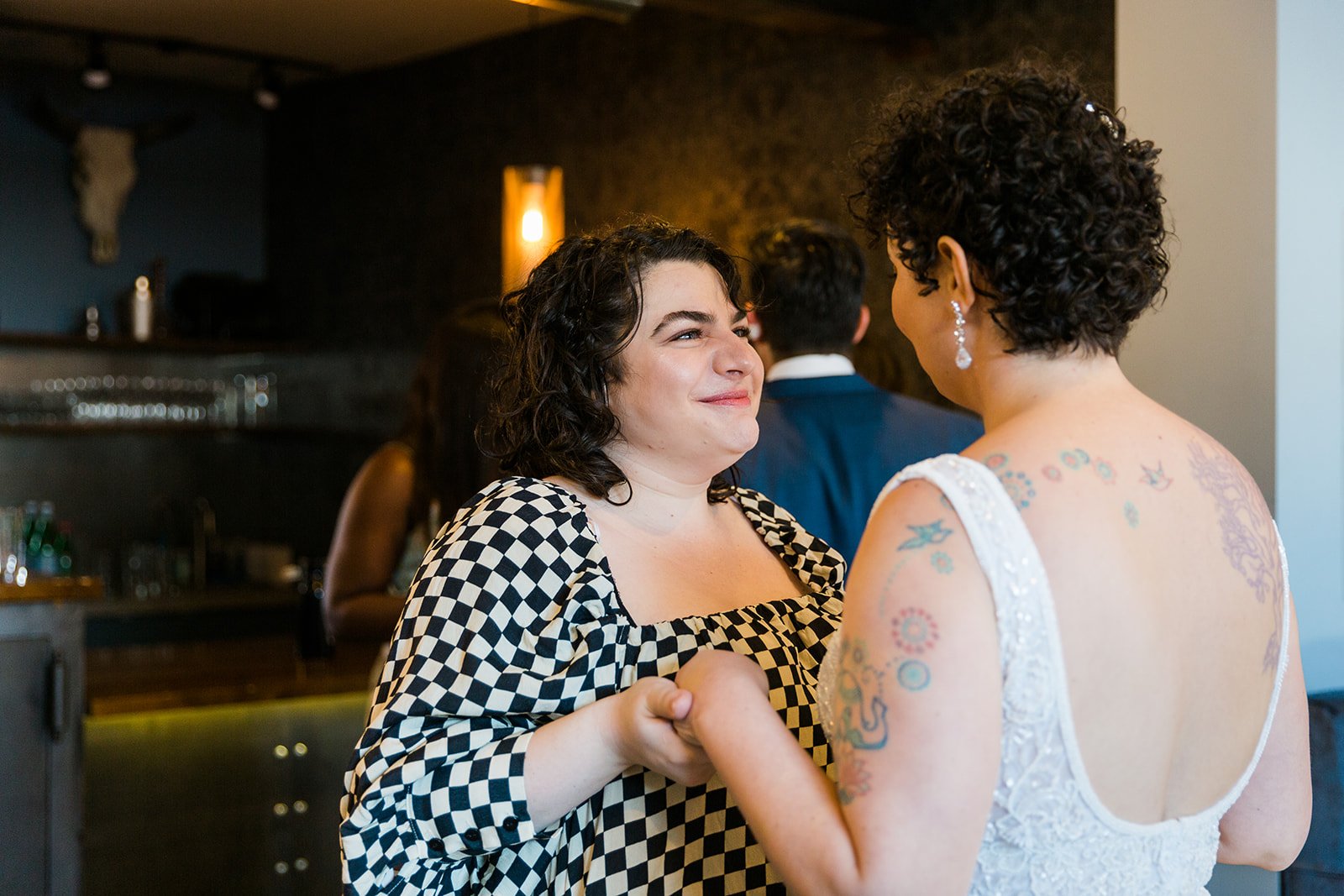  Documentary candid photo of a friend holding the brides hands before nontraditional queer, Jewish and Venezuelan wedding ceremony at The Joinery Chicago in Logan Square. 