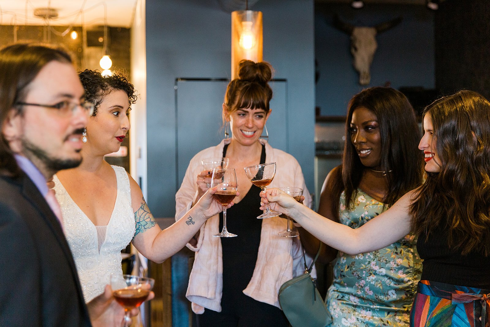  Documentary candid photo of a Diverse group of friends cheers with cocktails before nontraditional queer, Jewish and Venezuelan wedding ceremony at The Joinery Chicago in Logan Square. 