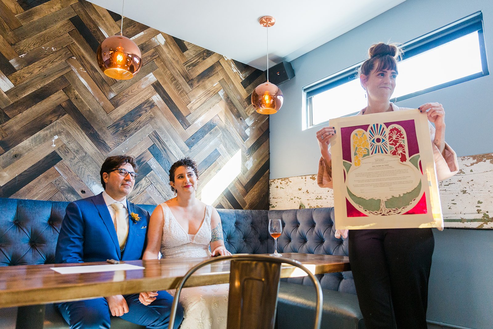  Documentary candid photo of the bride, groom and officiant during their ketubah signing before nontraditional queer, Jewish and Venezuelan wedding ceremony at The Joinery Chicago in Logan Square. 