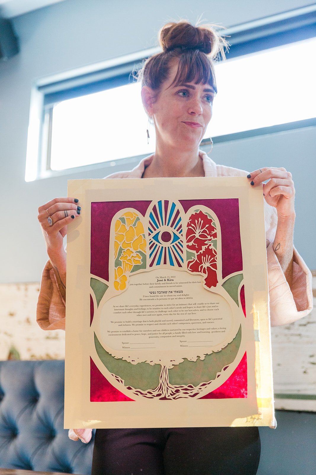  Documentary candid photo of wedding officiant and friend holding up the queer, nontraditional couples unique ketubah made by another friend at The Joinery Chicago in Logan Square.  