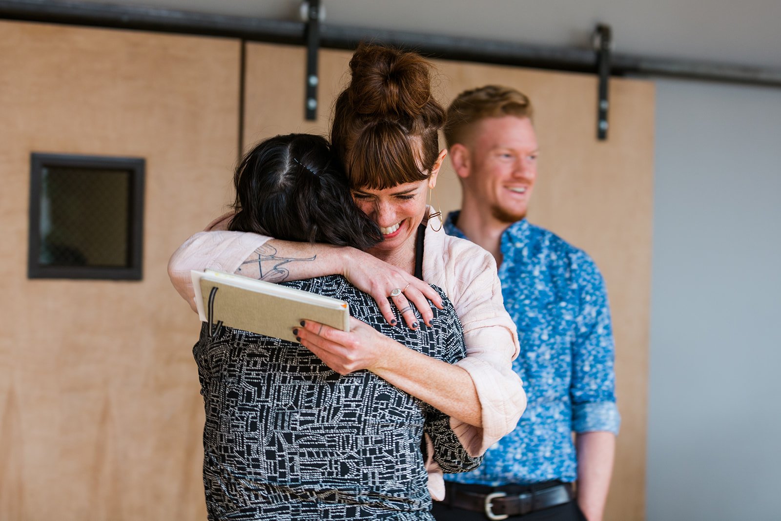  Candid documentary photo of diverse wedding guests hugging before nontraditional Jewish and Venezuelan wedding ceremony at The Joinery Chicago an Industrial loft wedding venue In Logan Square. 