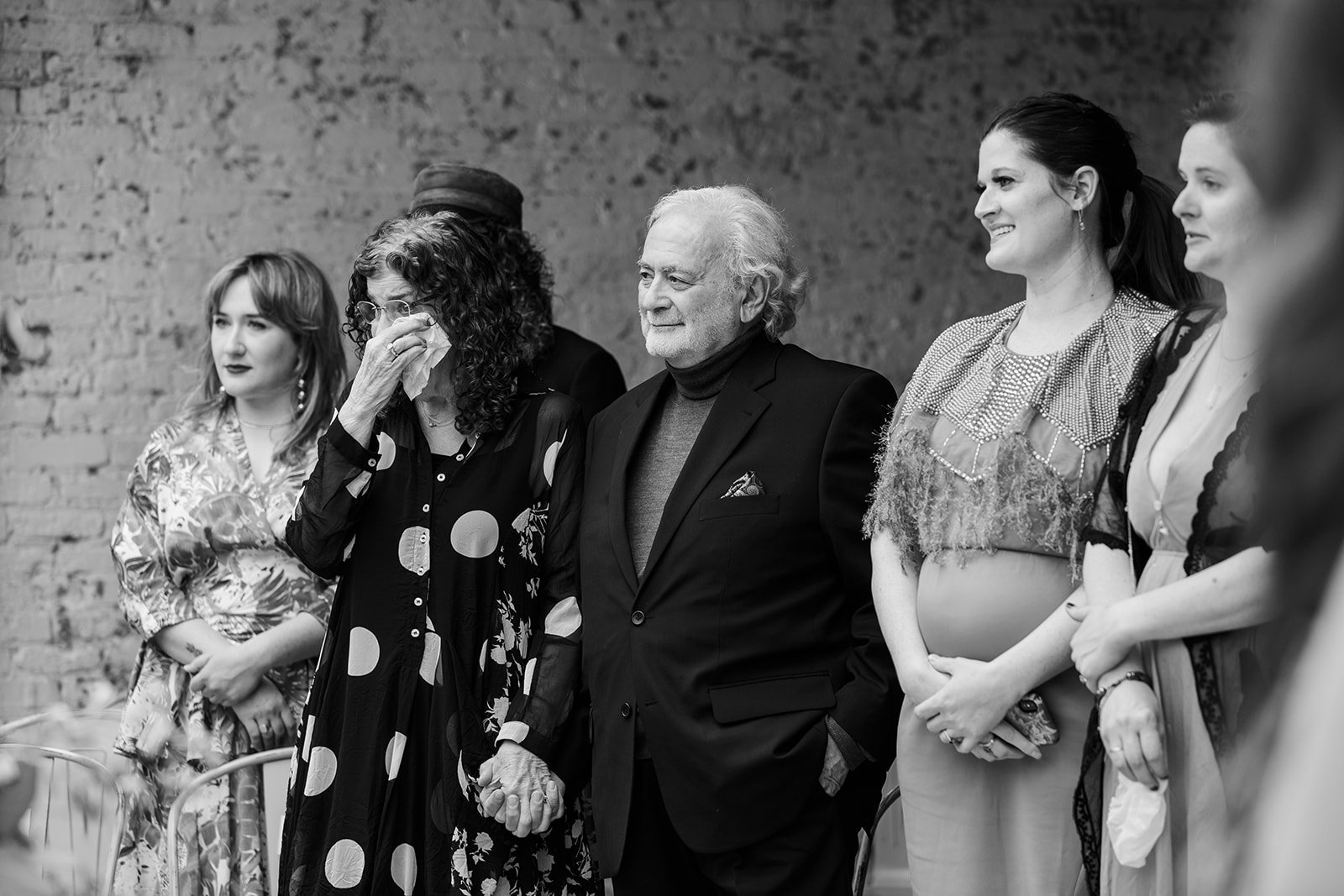  black and white, Candid, documentary photo of guests emotionally reacting to the bride and groom entering their nontraditional Jewish and Venezuelan wedding ceremony in the round at The Joinery Chicago an Industrial loft wedding venue In Logan Squar