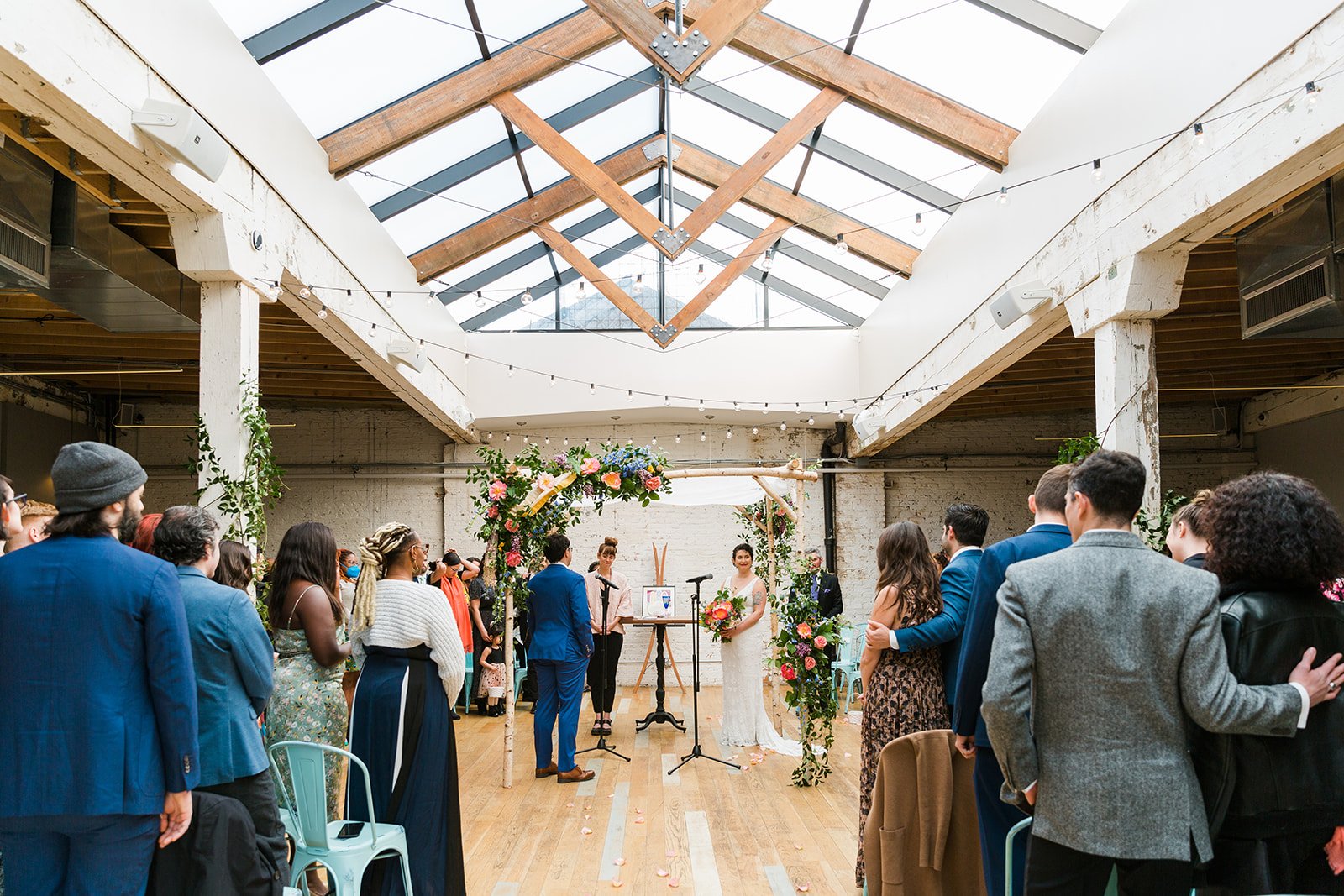  Candid, documentary wide photo bride and groom under chupah surrounded by guests during their nontraditional Jewish and Venezuelan wedding ceremony in the round at The Joinery Chicago an Industrial loft wedding venue In Logan Square. 