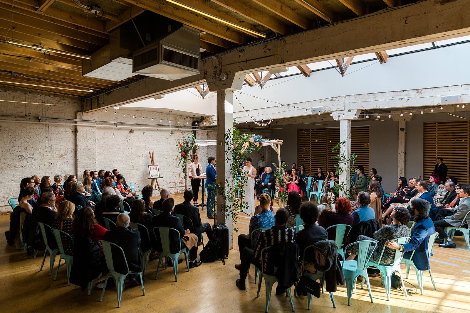  Candid, documentary wide photo bride and groom under chupah surrounded by guests during their nontraditional Jewish and Venezuelan wedding ceremony in the round at The Joinery Chicago an Industrial loft wedding venue In Logan Square. 