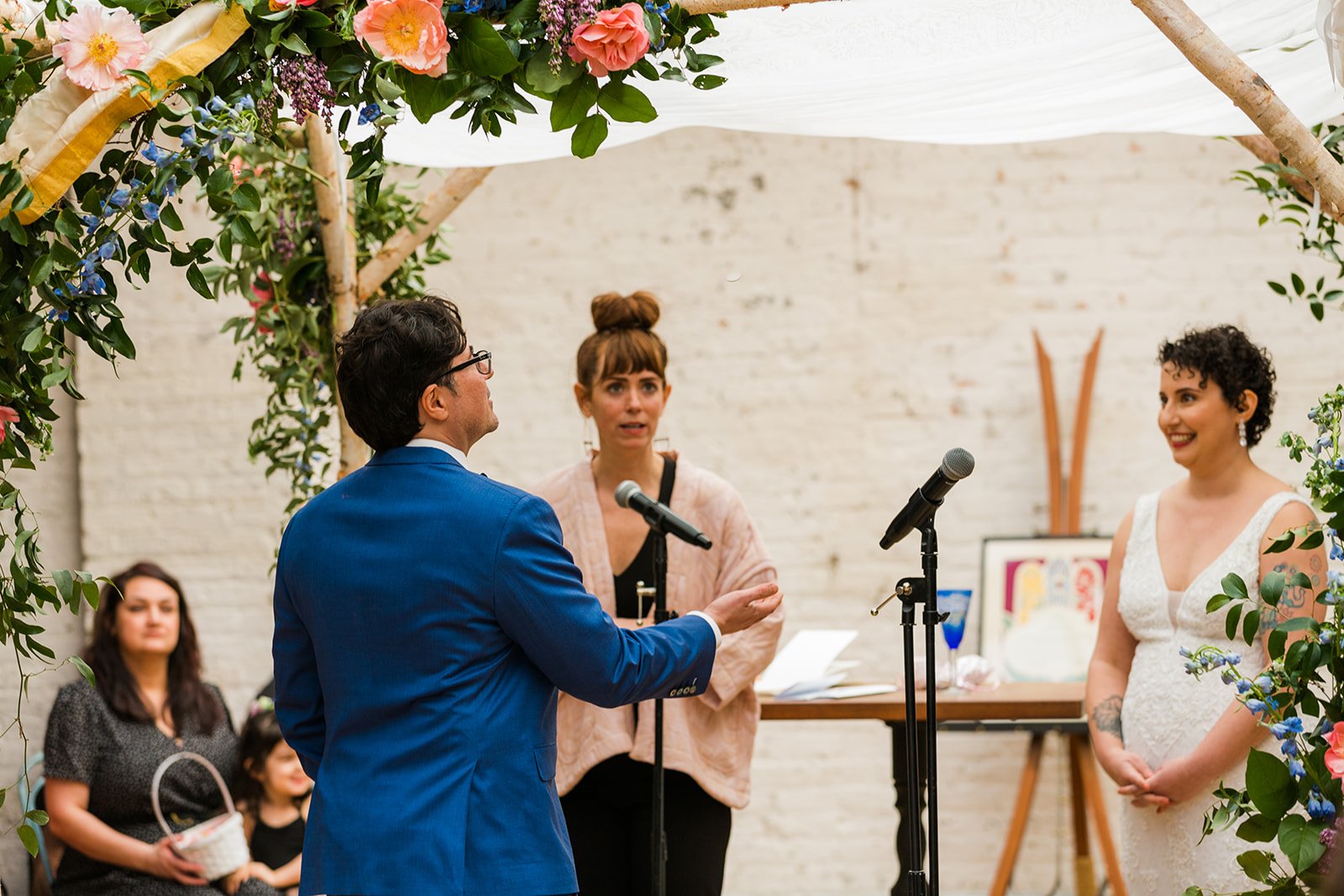  Candid, documentary photo of the groom flipping a coin to see who goes first in vow reading under the chupah during their nontraditional Jewish and Venezuelan wedding ceremony in the round at The Joinery Chicago an Industrial loft wedding venue In L