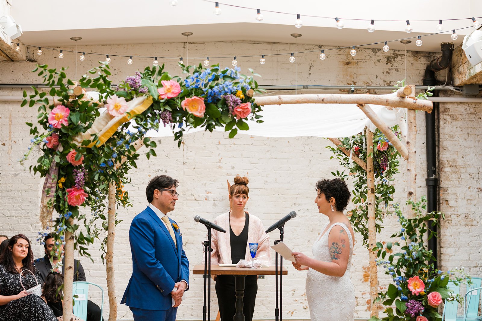  Candid, documentary photo of the bride reading their vows to the groom under chupah during their nontraditional Jewish and Venezuelan wedding ceremony in the round at The Joinery Chicago an Industrial loft wedding venue In Logan Square. 