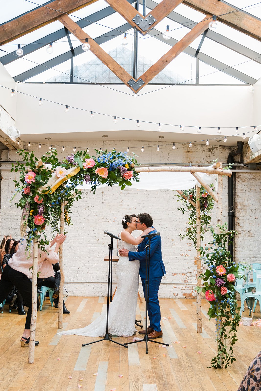  Candid, documentary photo of the couple kissing under chupah during their nontraditional Jewish and Venezuelan wedding ceremony in the round at The Joinery Chicago an Industrial loft wedding venue In Logan Square. 