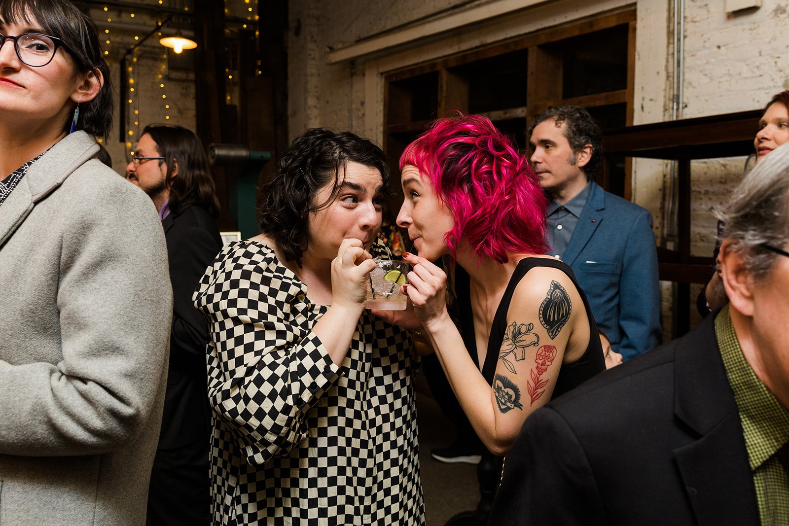  Candid documentary photo of diverse, queer wedding guests sharing a drink during cocktail hour after nontraditional Jewish and Venezuelan wedding ceremony at The Joinery Chicago an Industrial loft wedding venue In Logan Square. 