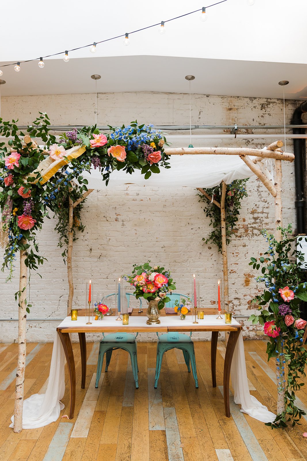  Documentary detail of wedding decor, head wedding sweetheart table with bright florals, tall colorful candles and airy white linens at nontraditional Jewish and Venezuelan wedding  at The Joinery Chicago an Industrial loft wedding venue In Logan Squ