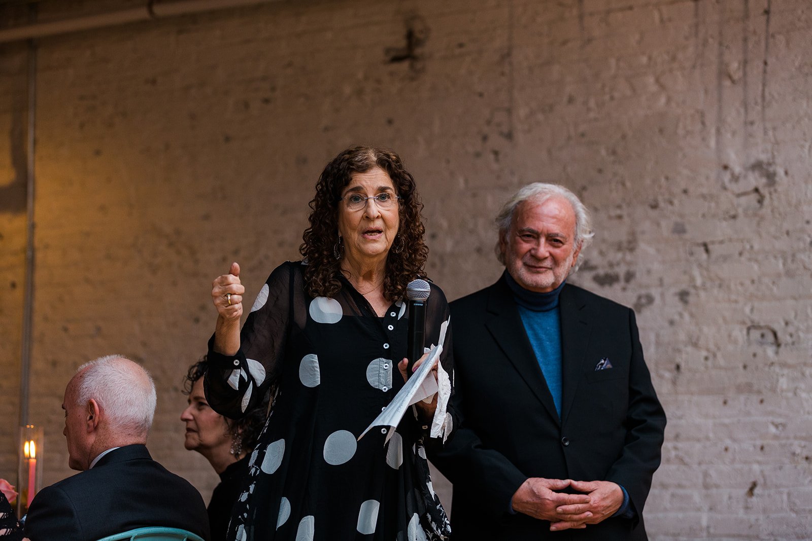  Documentary candid photo of bride’s parents giving a toast during the reception at nontraditional Jewish and Venezuelan wedding at The Joinery Chicago an Industrial loft wedding venue In Logan Square.  