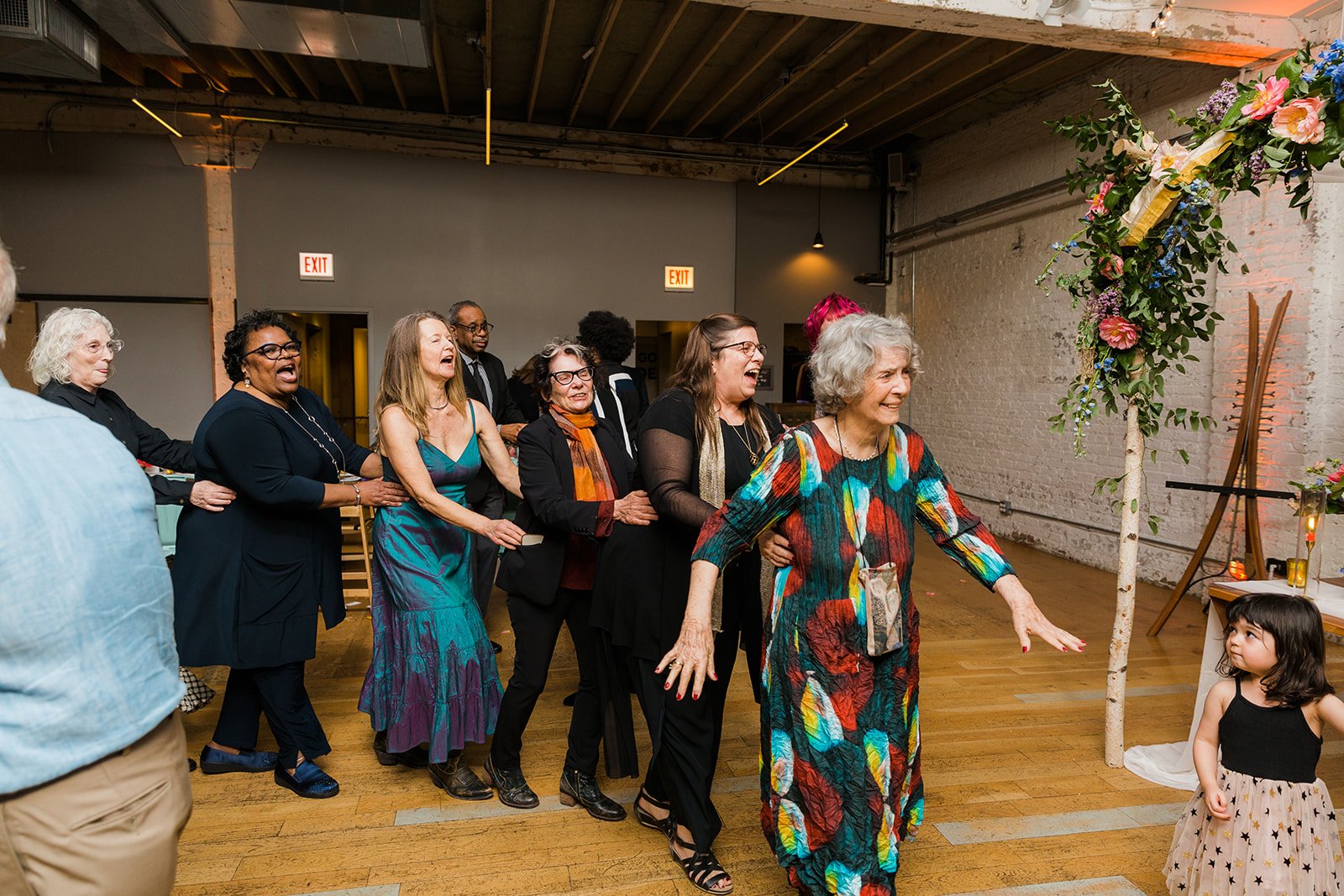  Documentary candid photo of a dance line of guests at nontraditional Jewish and Venezuelan wedding at The Joinery Chicago an Industrial loft wedding venue In Logan Square.  