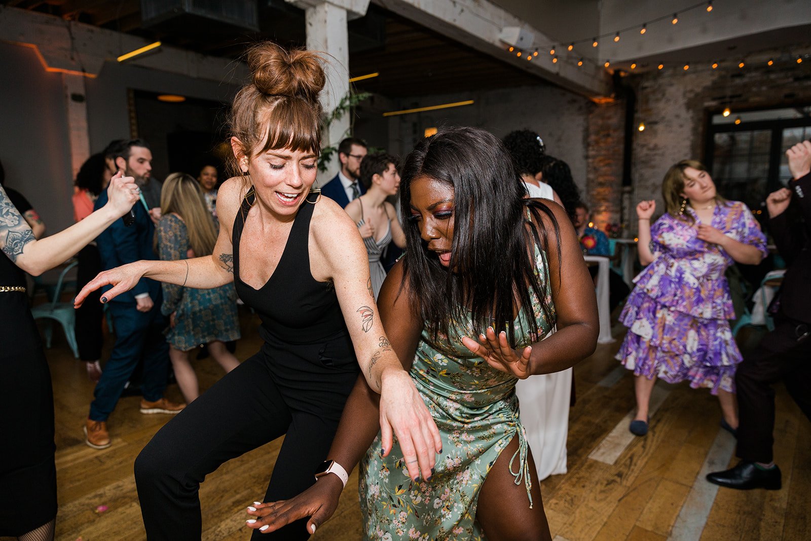  Documentary candid photo of diverse guests dancing at nontraditional Jewish and Venezuelan wedding reception at The Joinery Chicago an Industrial loft wedding venue In Logan Square.  