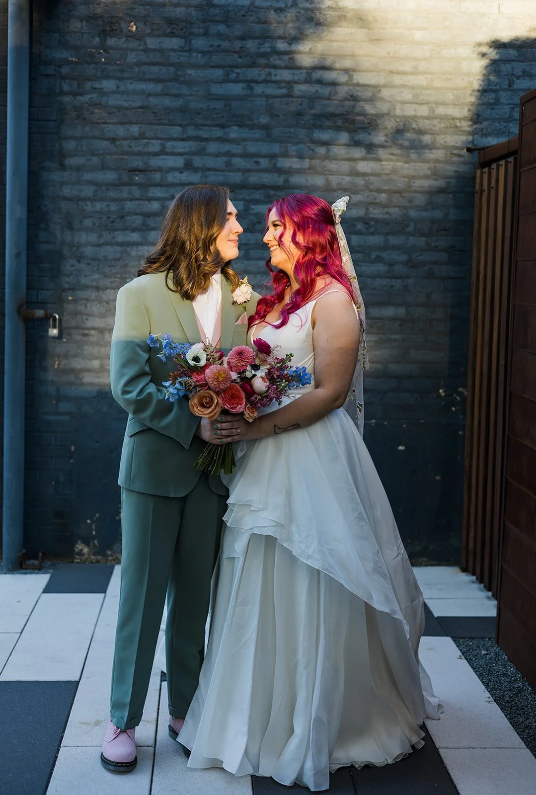  Portrait of nontraditional, queer brides, one in a white dress the other in a light green suit in front of The Joinery in Logan Square, one of the most LGBTQ friendly wedding venues in Chicago.  