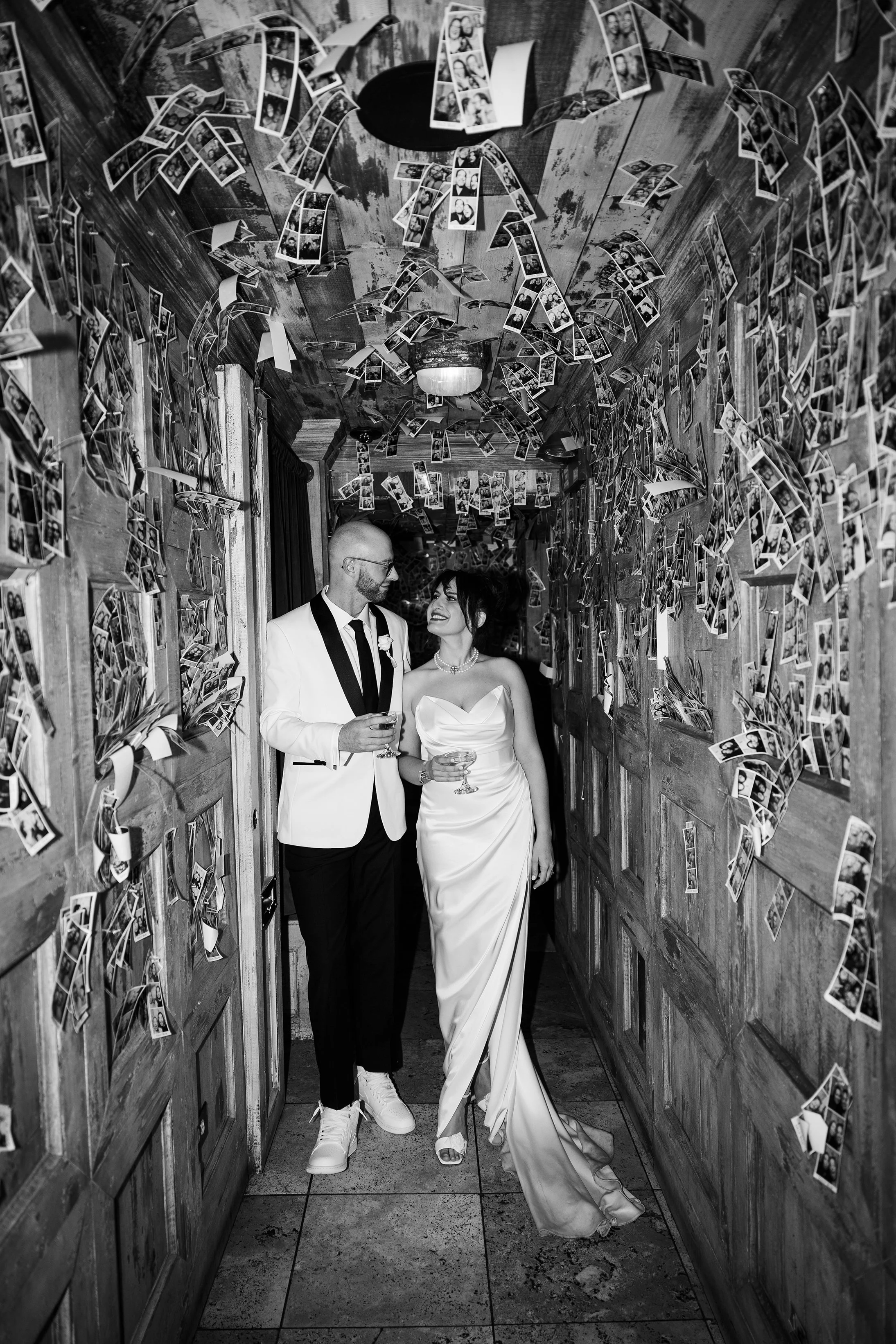  Black and white documentary style wedding portrait of bride and groom with cocktails in the photo booth strip hallway at  Gilt Bar Chicago wedding 