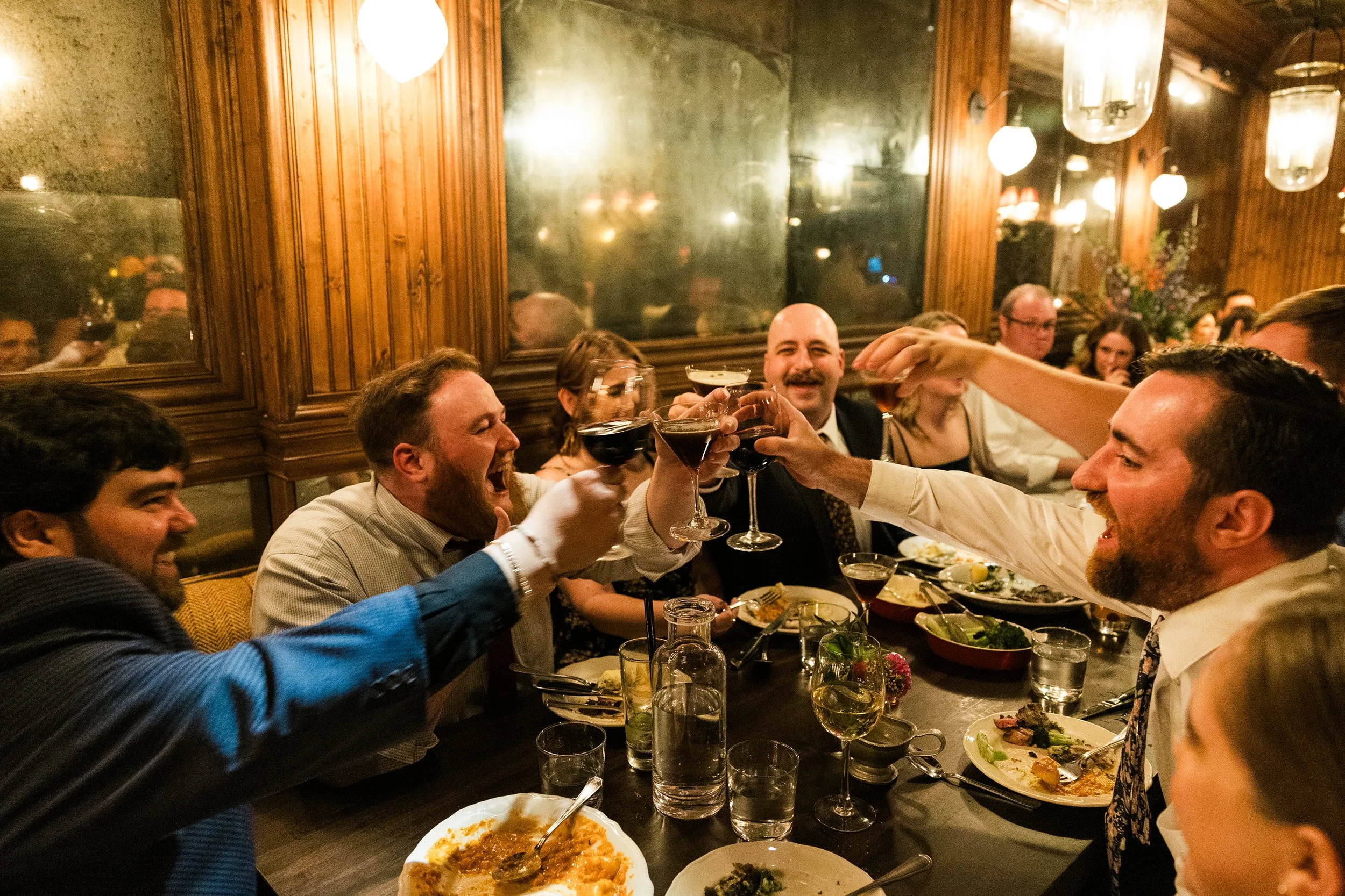  Documentary style candid photo of guests cheering with cocktails at romantic, candle lit restaurant / bar wedding reception at Gilt Bar Chicago 