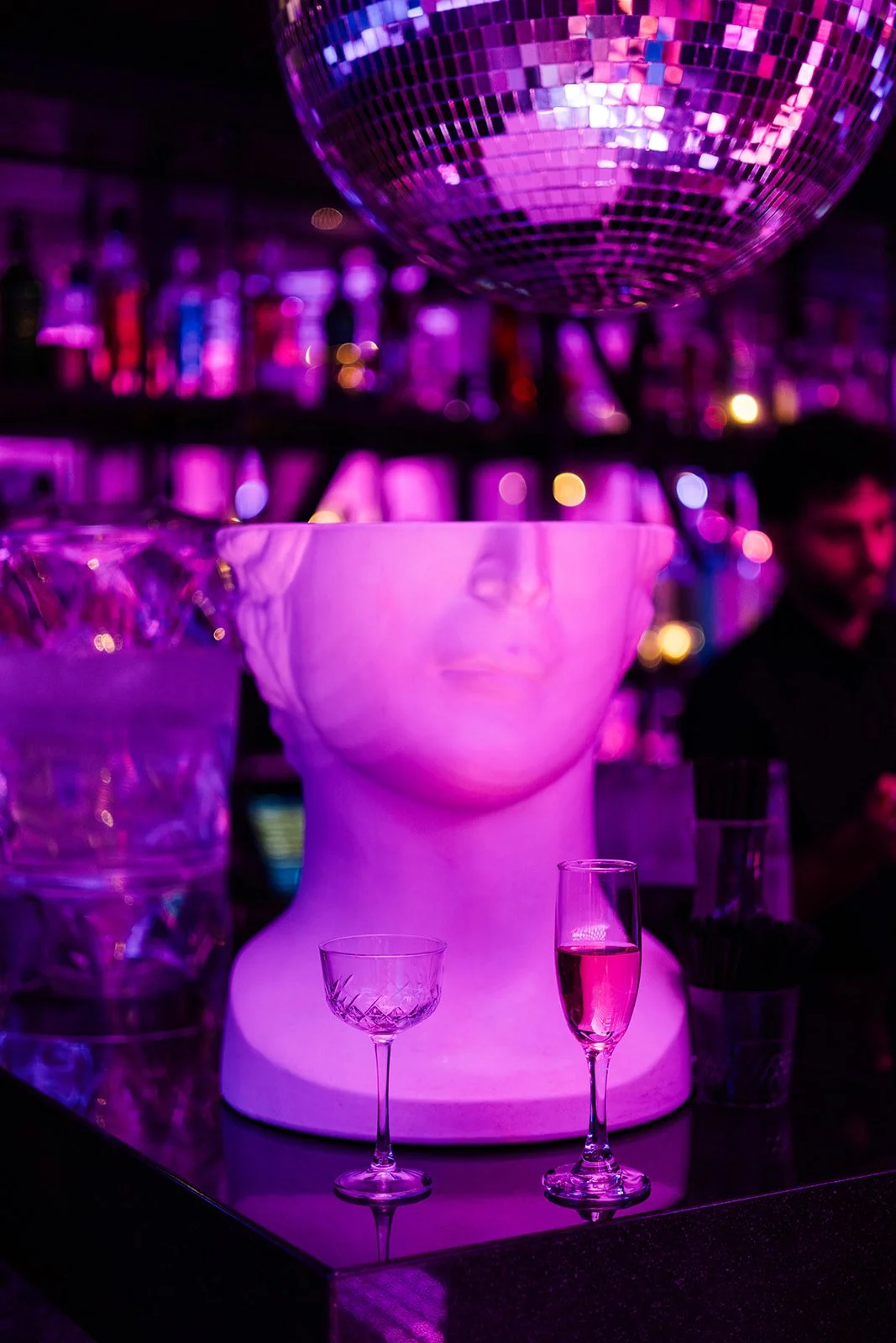  Documentary style portrait of a bride sitting on the grooms lap in a disco ball chair on a neon purple lit dance floor at their nontraditional wedding at Disco Celeste. Bar / restaurant wedding venue inspiration.  