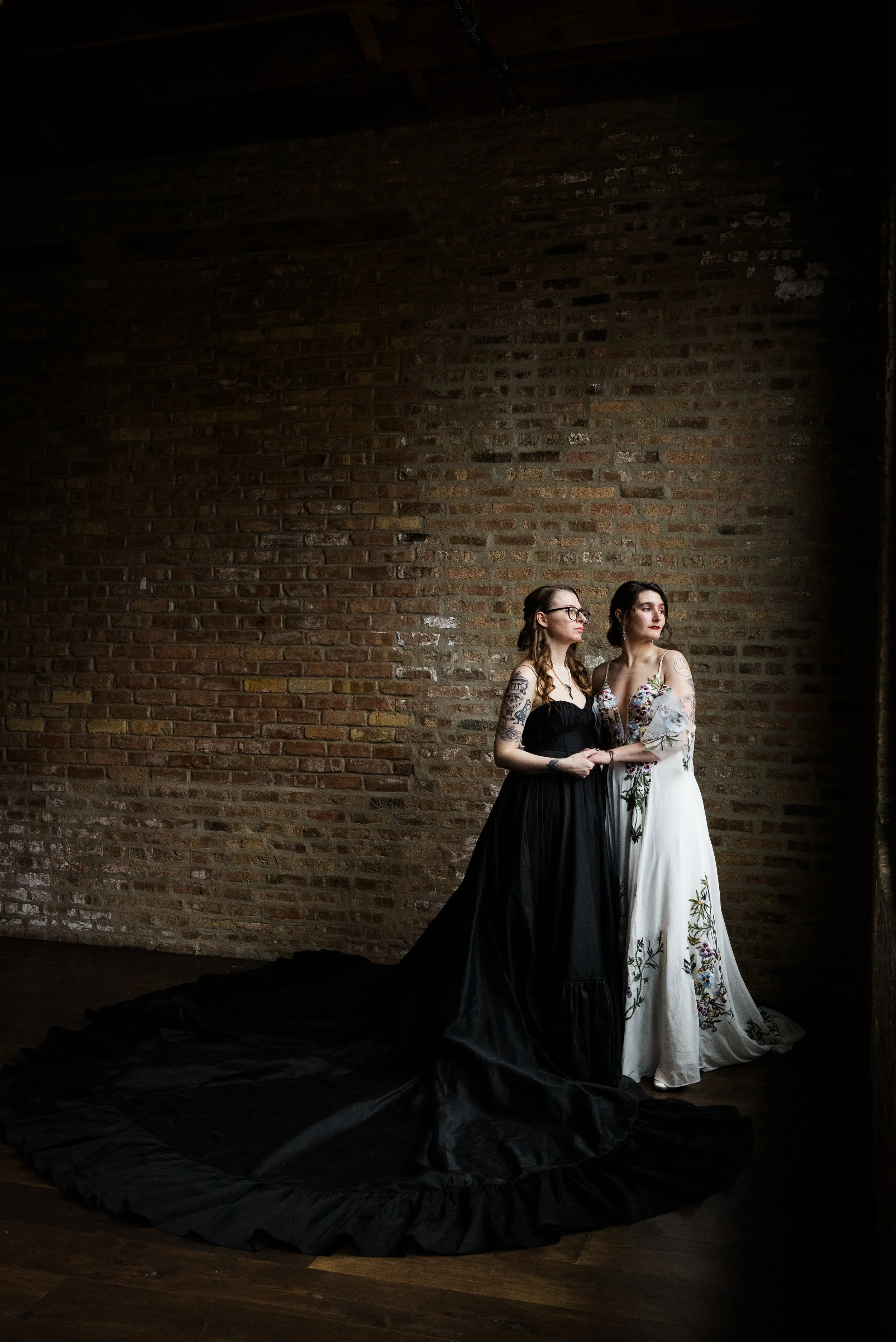 Moody documentary style portrait of brides in black and white dramatic dresses at nontraditional queer wedding at Ravenswood Event Center Chicago