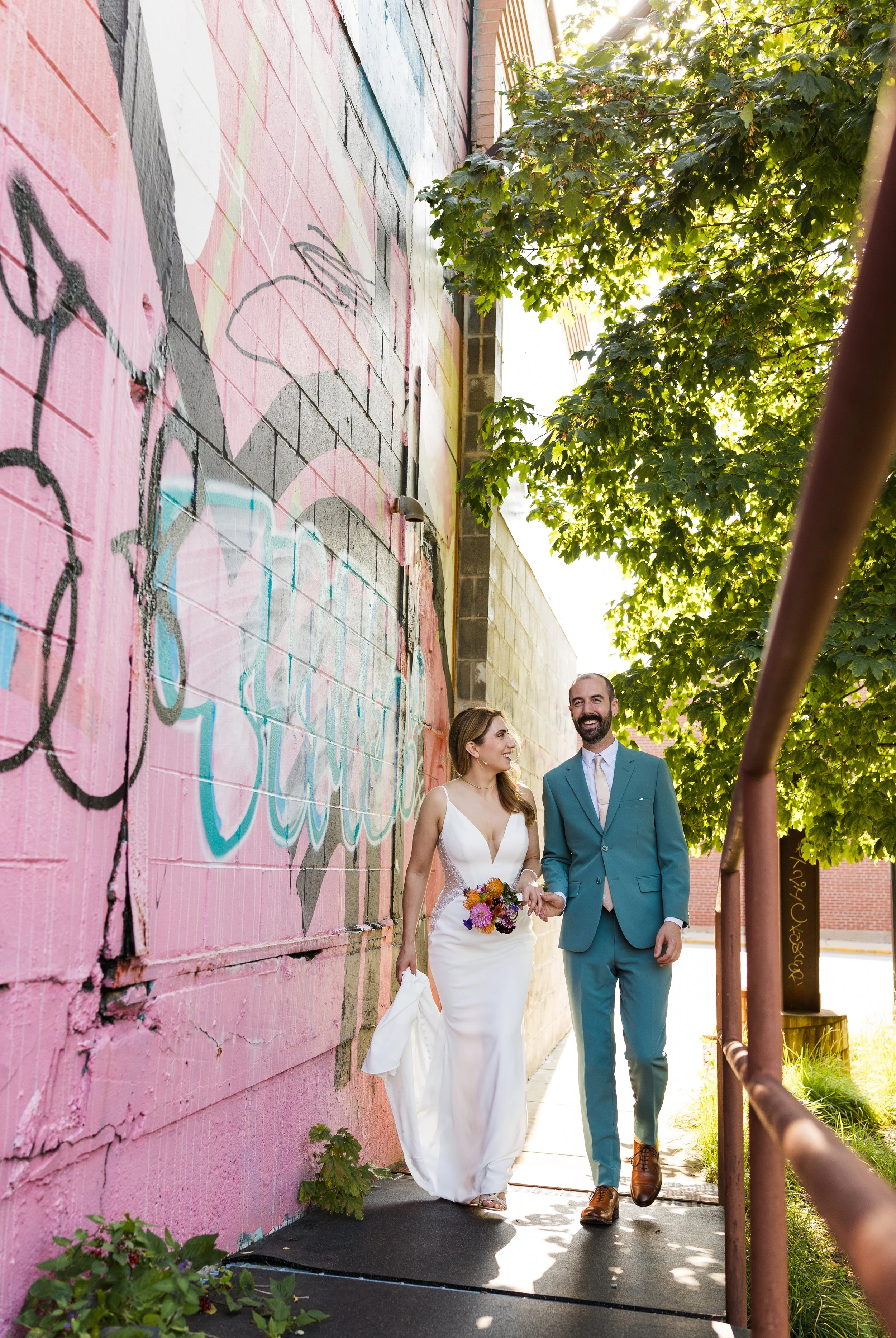 Documentary style portrait of a bride and groom walking by a graffiti wall on their intimate wedding day