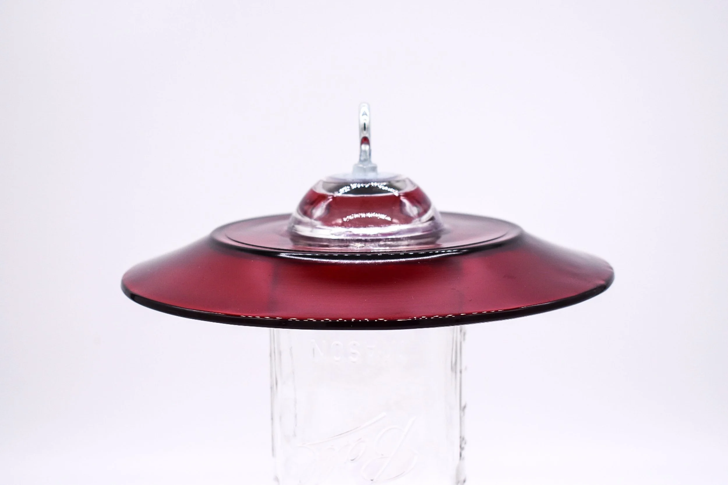 Close-up of the red glass bird feeder rain guard and hanging hardware showing the vintage glass construction.