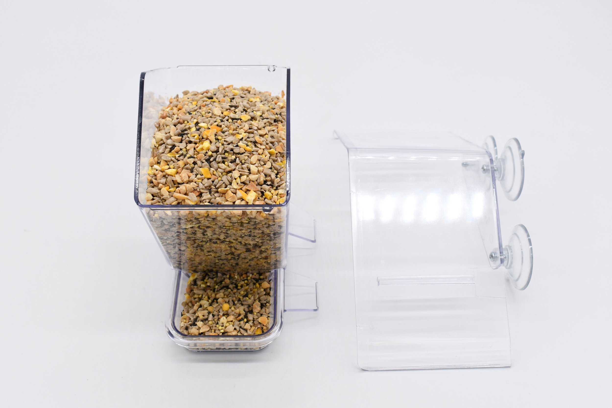 Side view of the Window Cafe bird feeder with filled seed reservoir and removable clear roof displayed beside it.