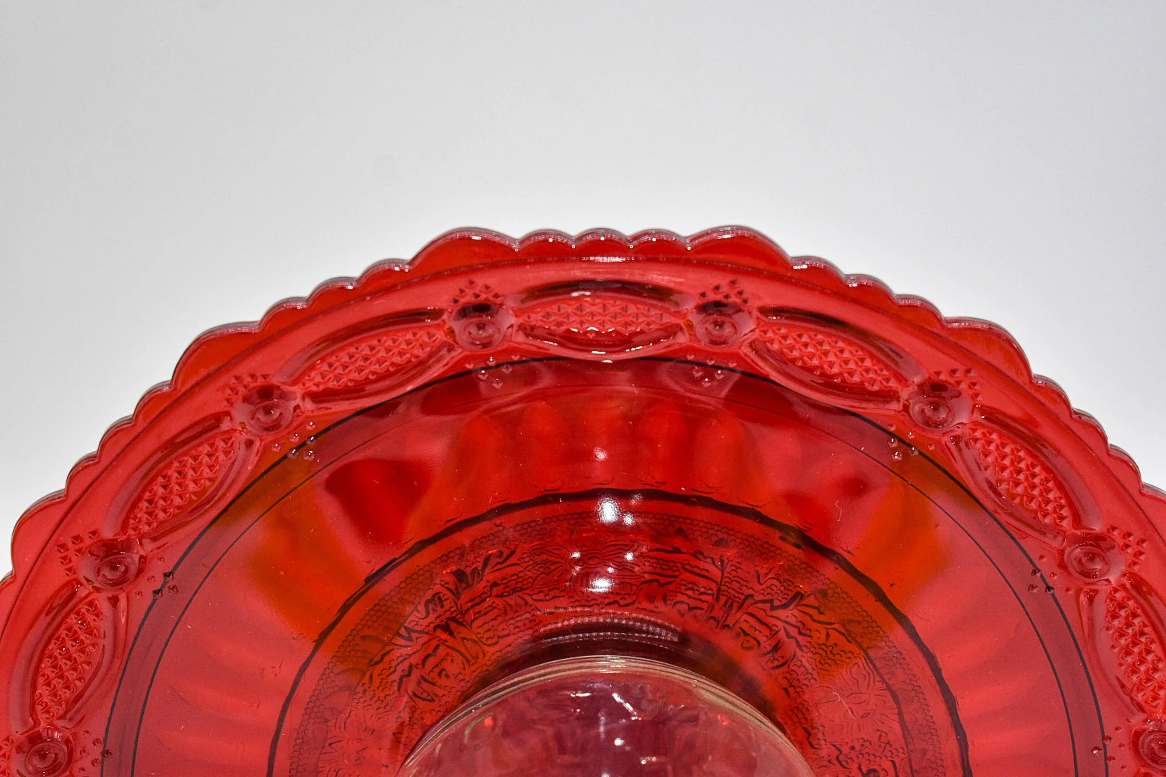 Extreme close-up of vintage Avon Cape Cod ruby red glass showing its scalloped edge, raised decorative pattern, and rich translucent red color.