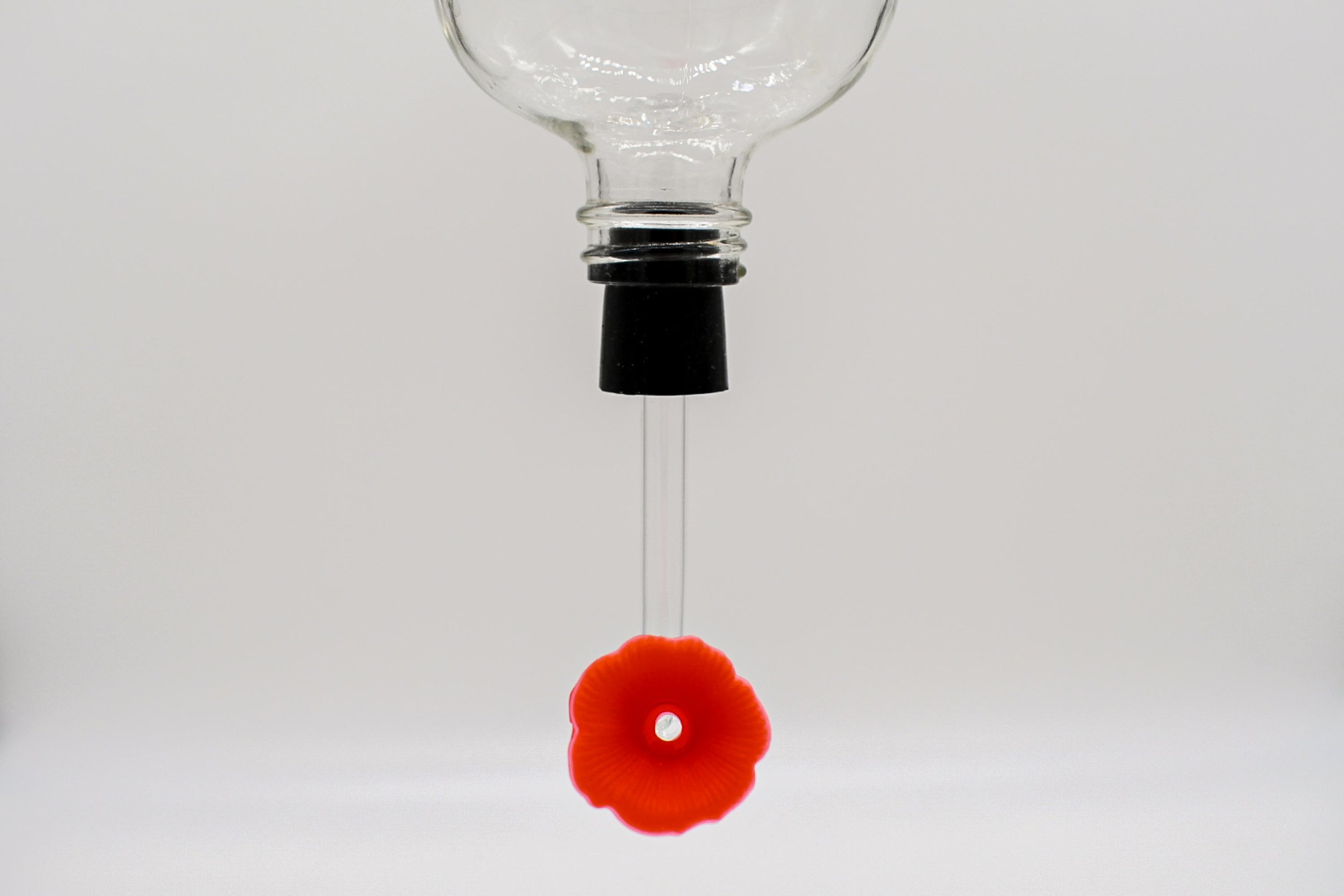 Hummingbird feeder replacement stopper and tube installed in a glass bottle with red flower feeding port