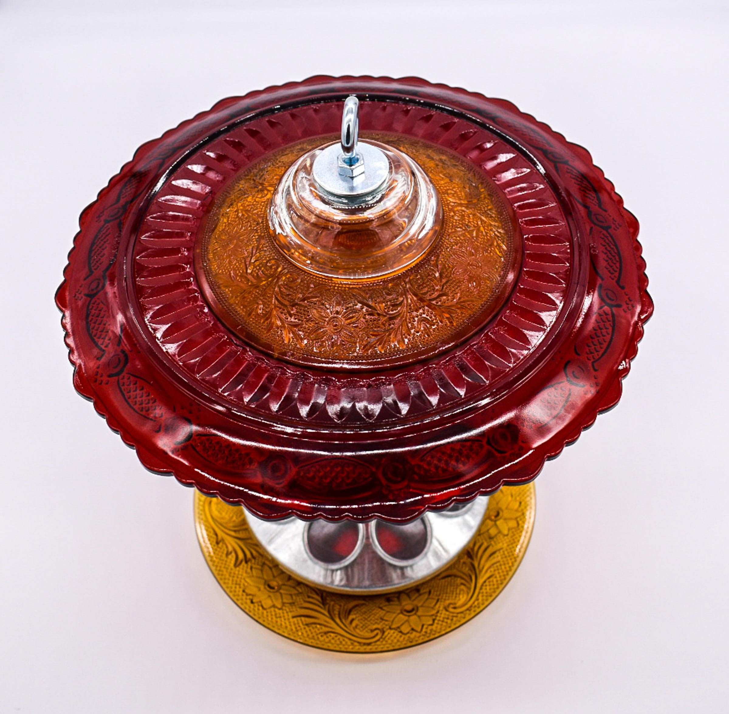 Overhead view of ruby red vintage glass bird feeder showing the amber glass saucer, decorative red plate, and silver hanging hardware.