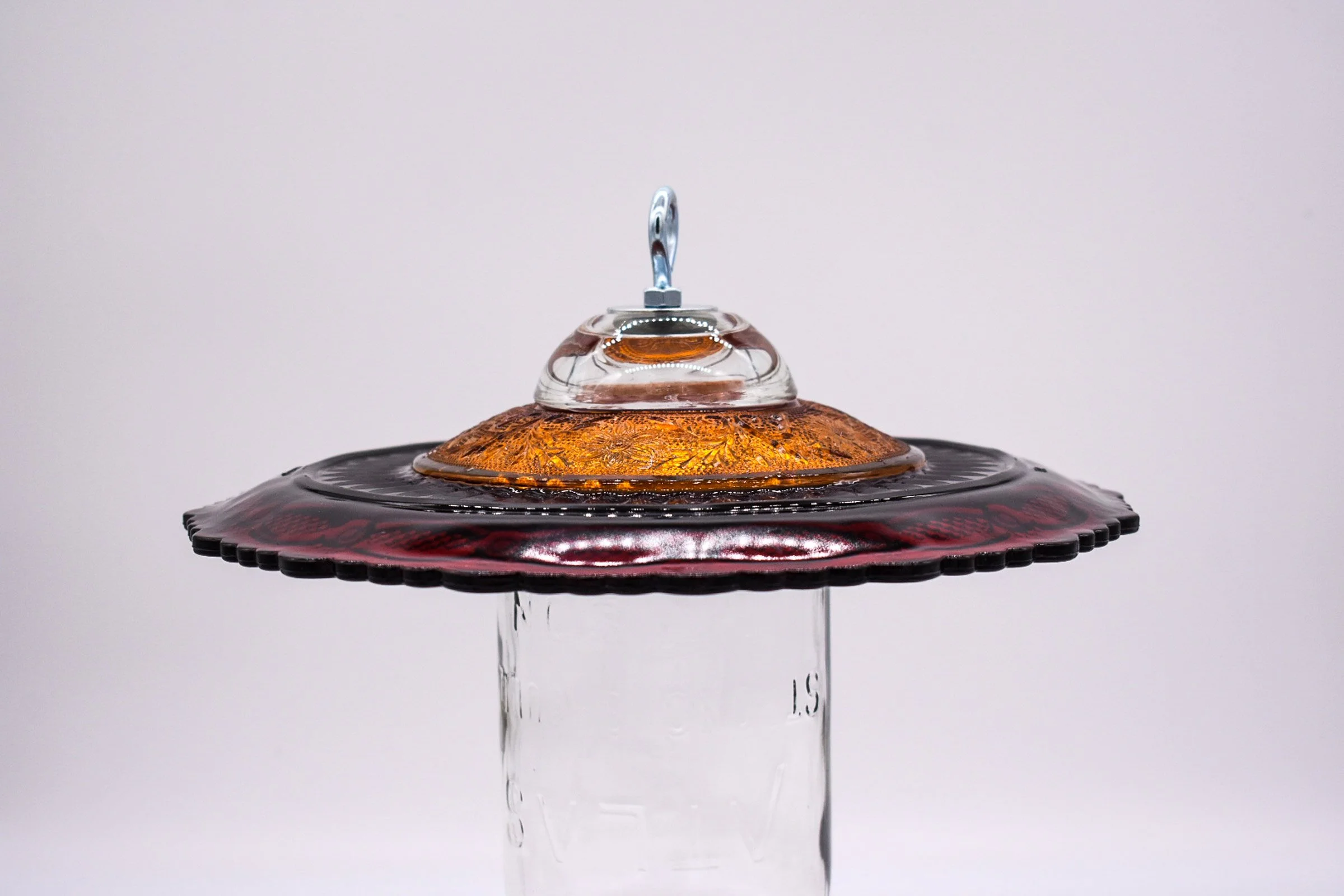 Side profile close-up of the ruby red Avon Cape Cod glass plate with an amber glass saucer mounted above it and metal hanging hardware.