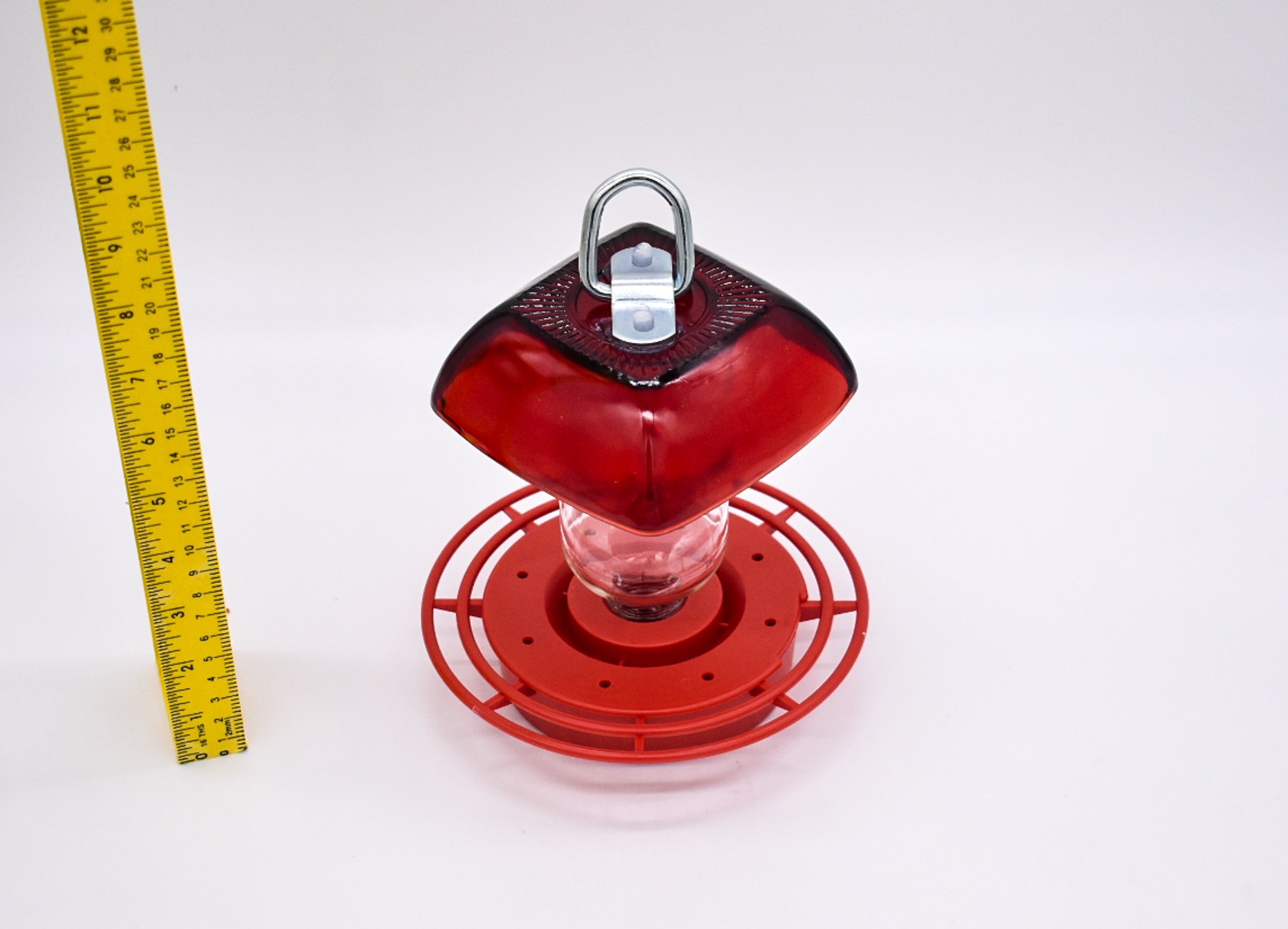 Side view of the Anchor Hocking Ruby Red Berry Bowl glass with 8 oz reservoir and red Best 1 plastic hummingbird feeder. A vertically placed ruler shows the feeder is approximately 7 inches tall.