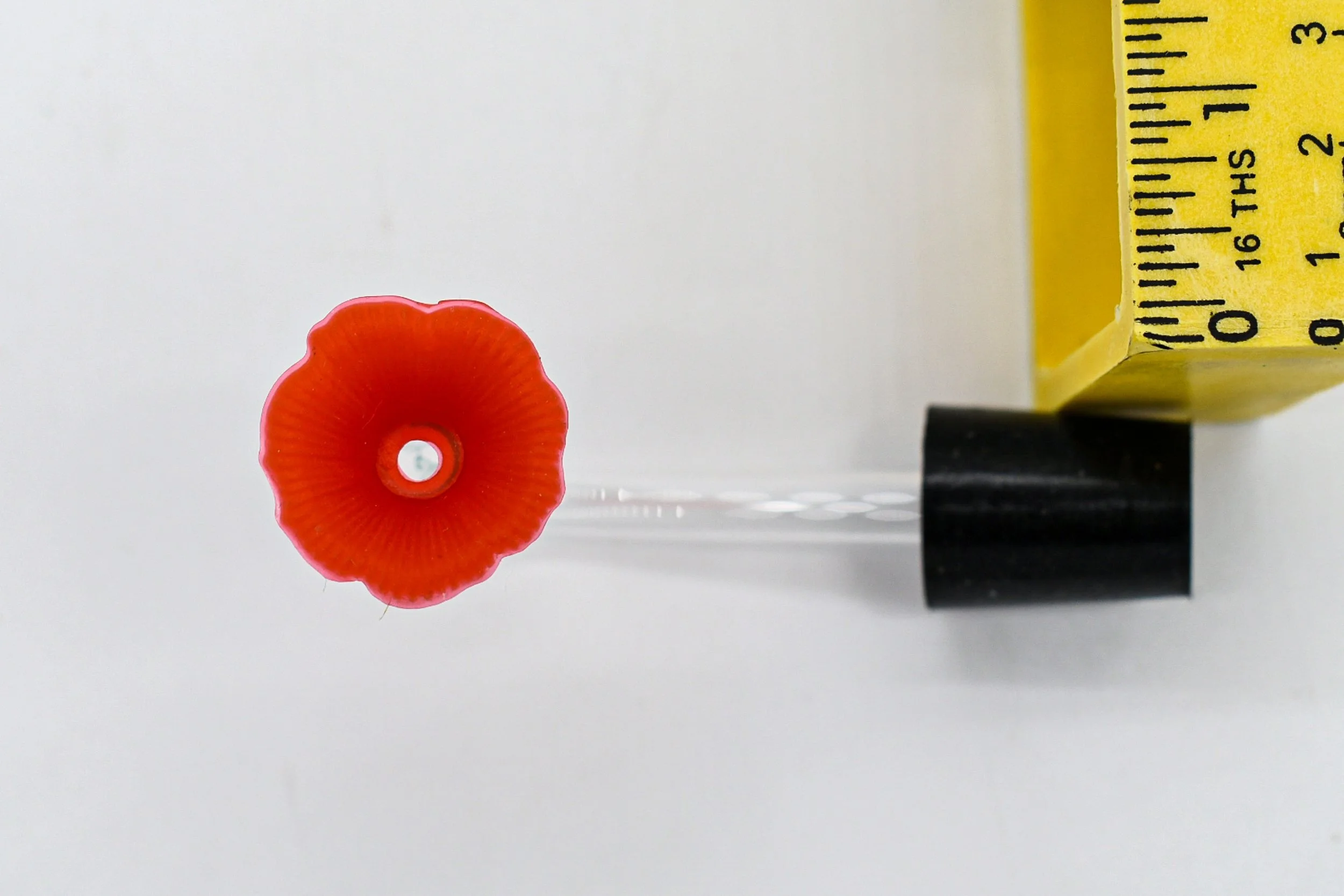 Red flower feeding port and clear hummingbird feeder replacement tube shown with measuring tape