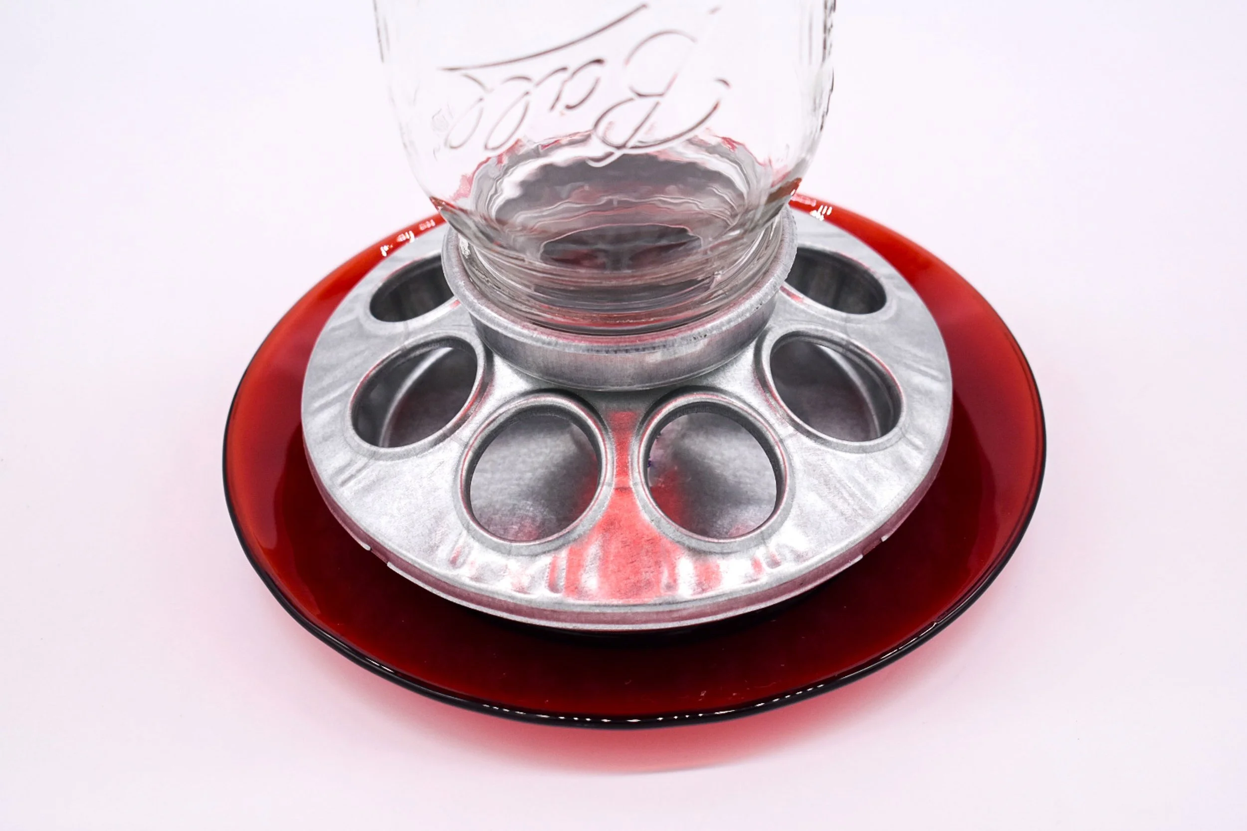 Close-up of galvanized metal seed feeding ports, Mason jar connection and red glass feeding tray on handmade bird feeder.