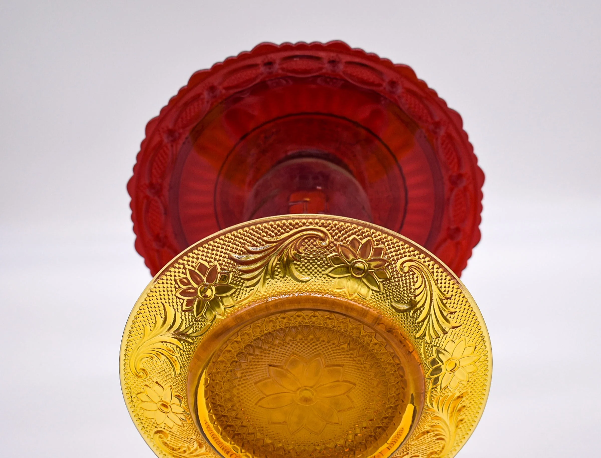 Close-up of the undersides of vintage ruby red and amber glass plates showing the molded floral designs and decorative glass patterns.