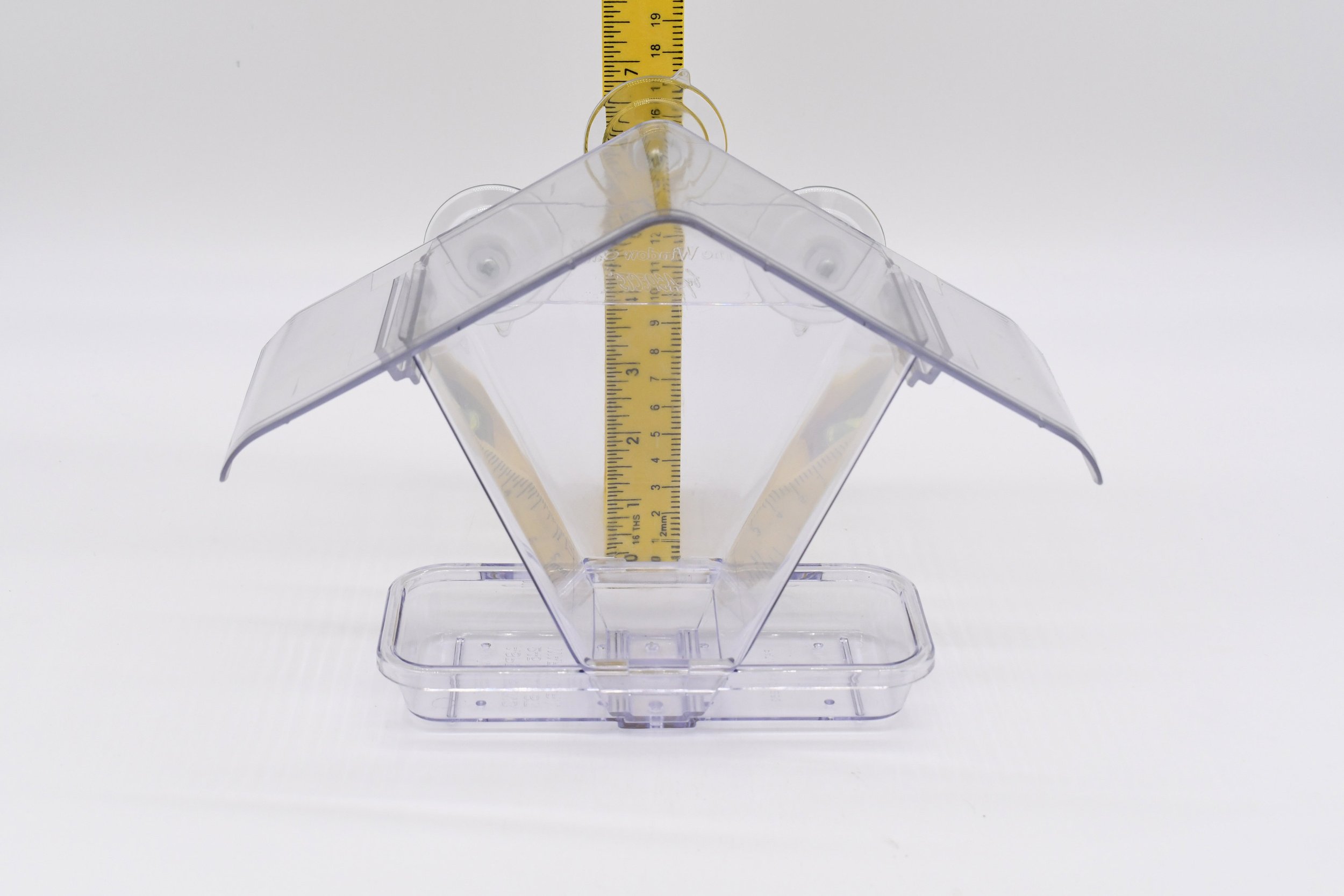Front view of the empty Aspects #155 Window Cafe bird feeder showing its clear roof, seed reservoir, and feeding tray beside a measuring ruler.