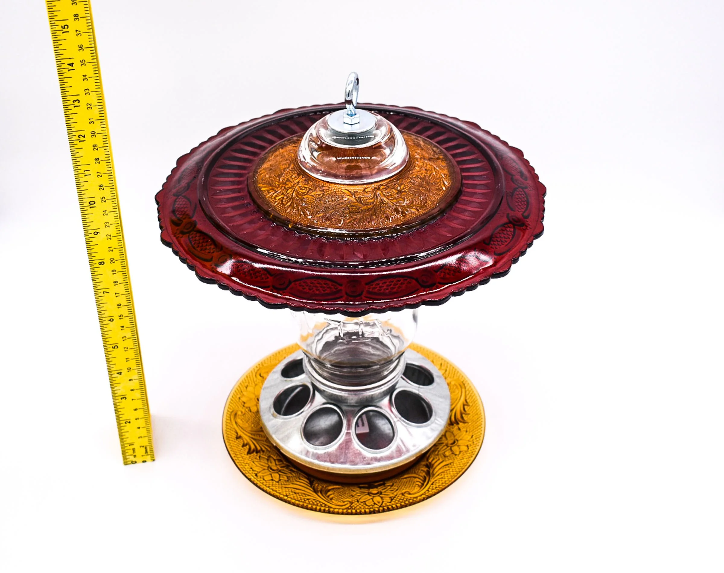 Angled view of handmade ruby red glass Mason jar bird feeder showing the layered vintage glass plates, silver seed feeding base, and amber lower tray.