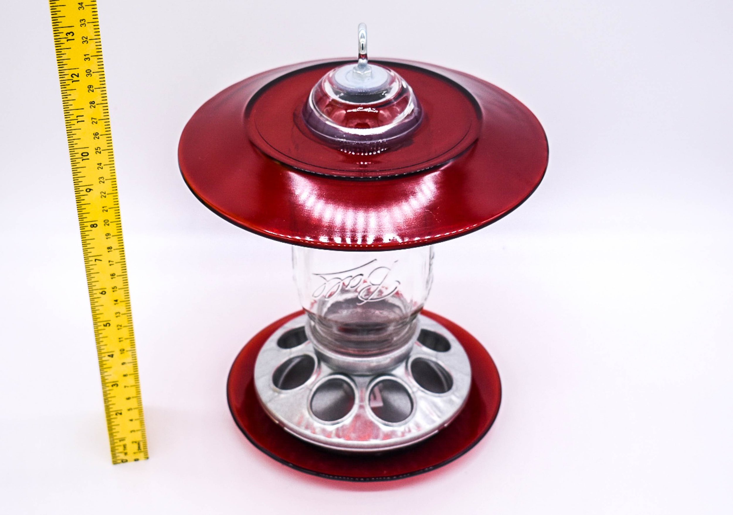 Angled view of red glass Mason jar seed bird feeder showing vintage glass roof, Mason jar and galvanized feeding base.