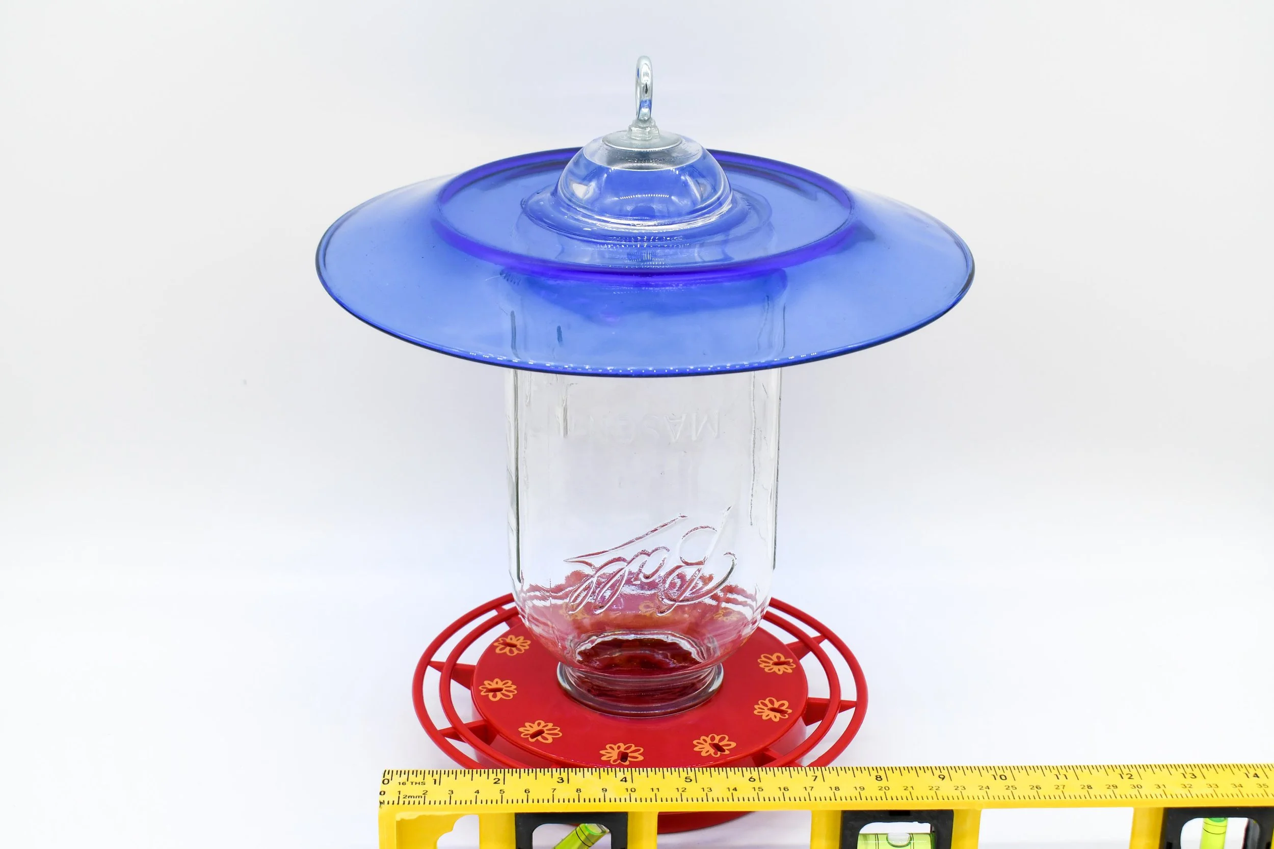 Bottom view of the cobalt glass feeder showing the red circular perch and feeding base with ruler showing width.