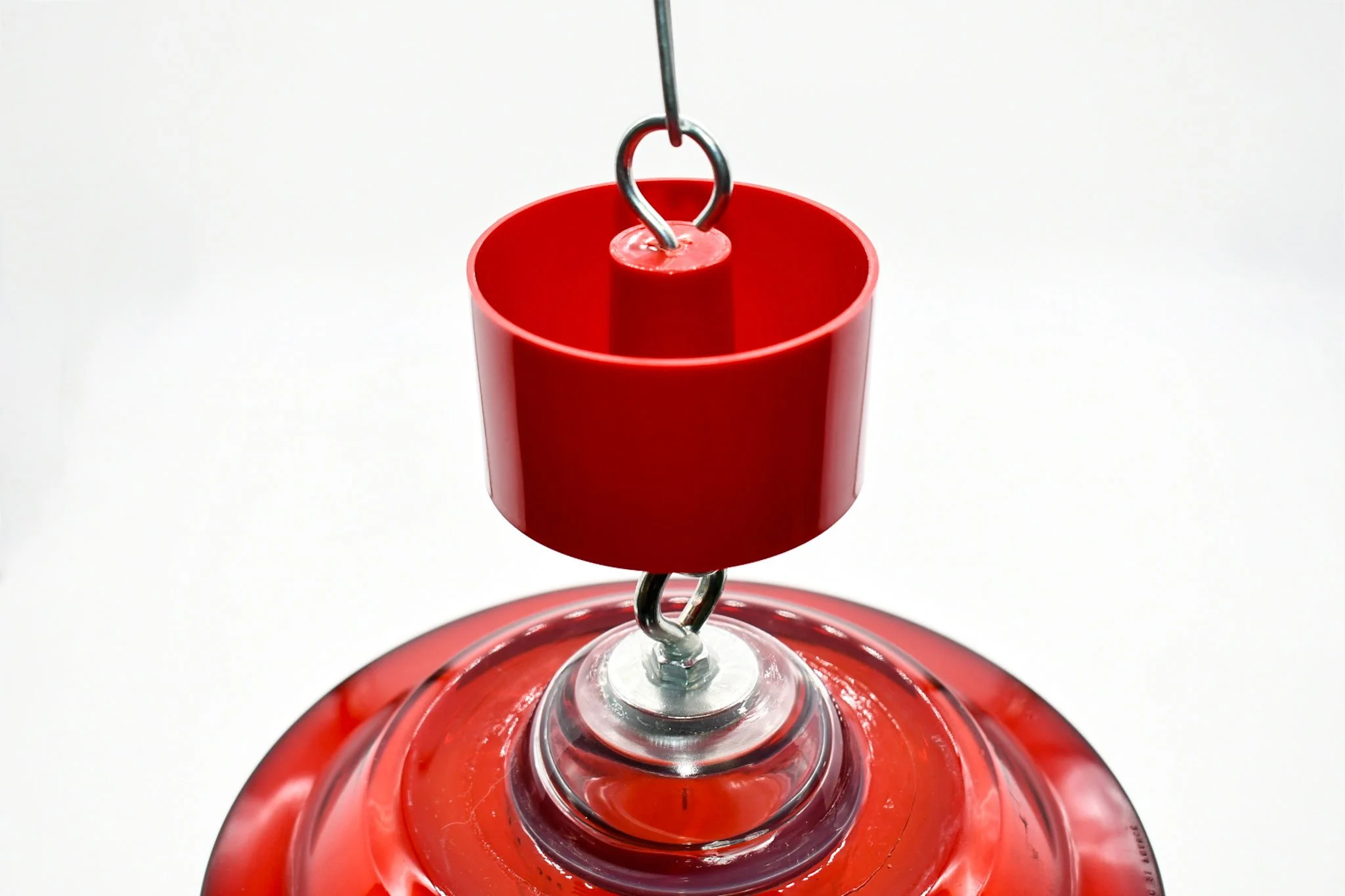 Close-up of a red ant trap attached to the upper hook of a hanging feeder.