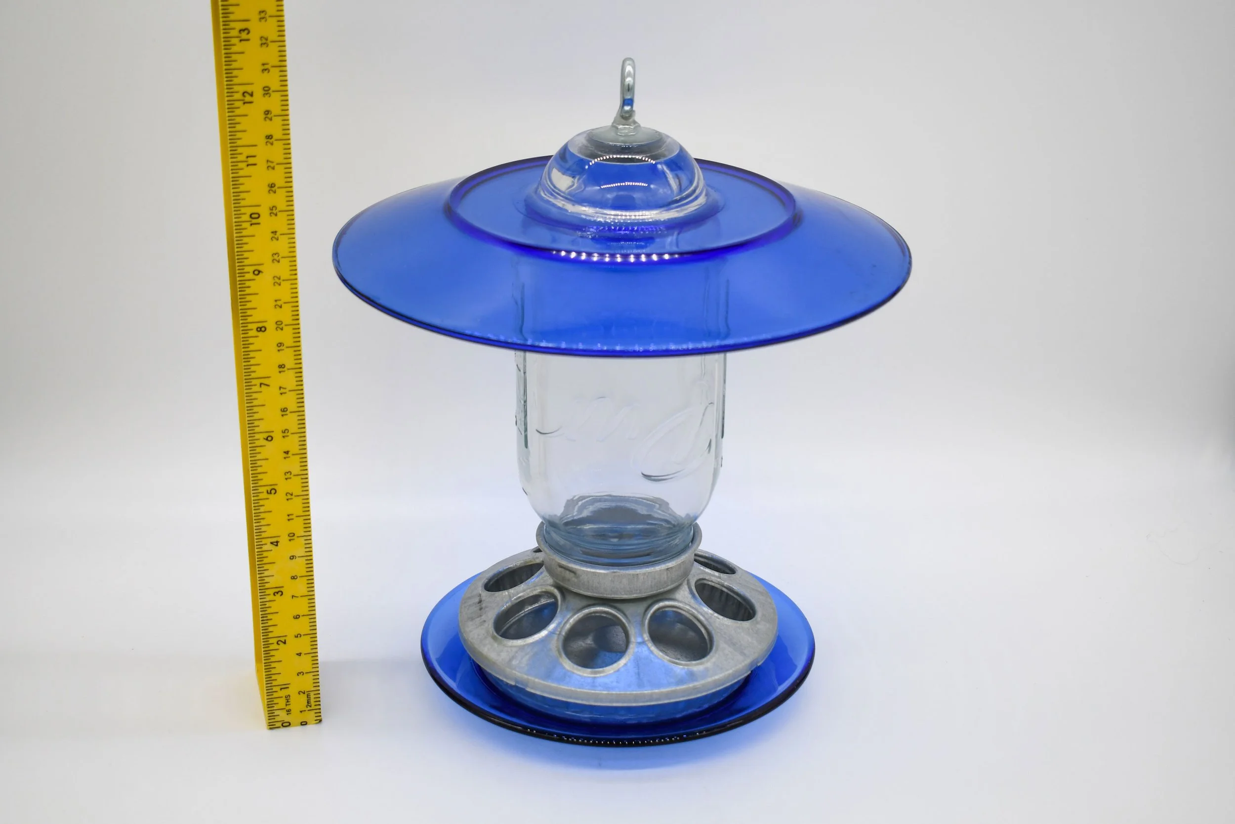Front view of royal blue glass Mason jar bird feeder beside ruler showing overall size