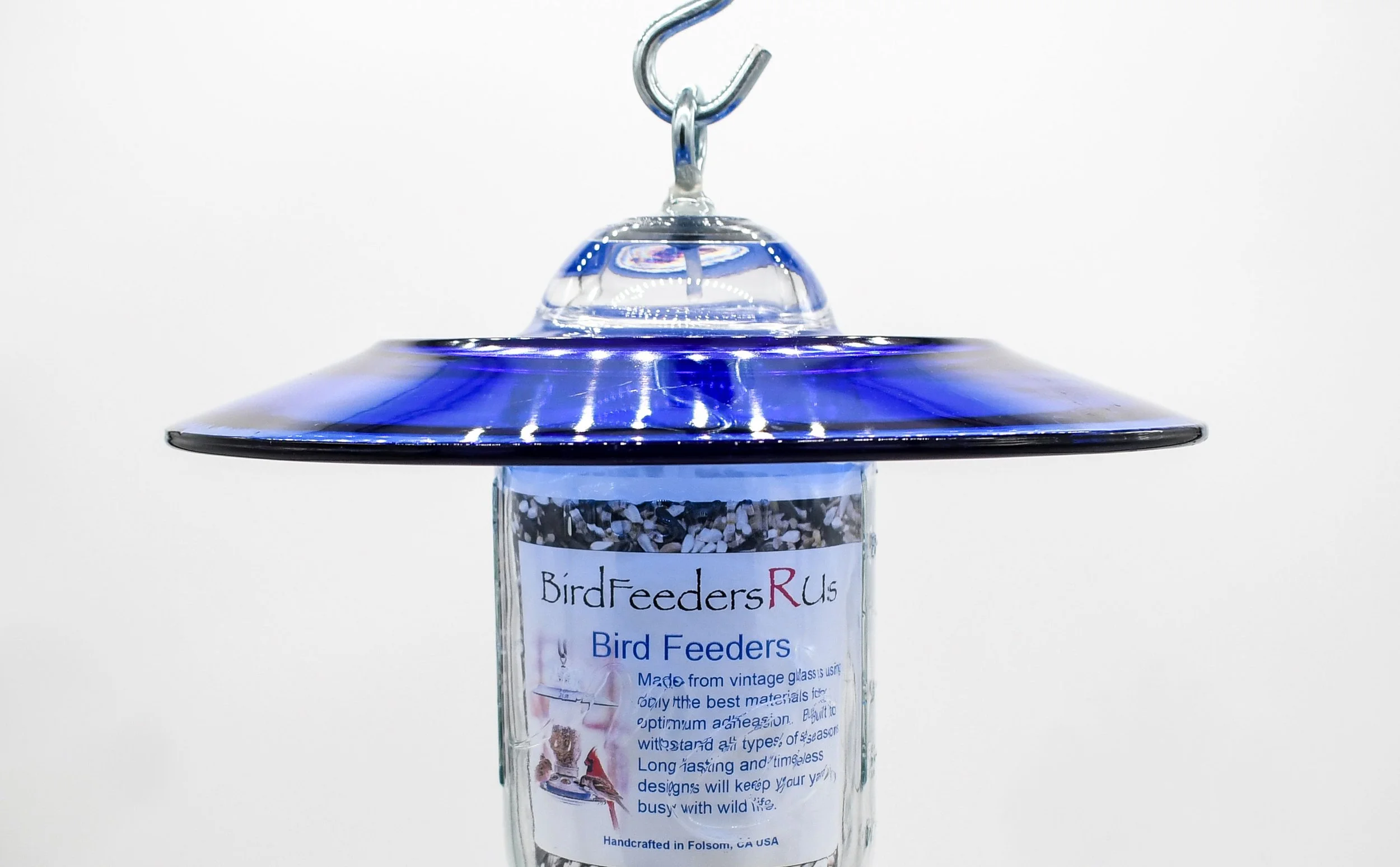Close-up of royal blue glass bird feeder showing hanging hook hardware and glass weather shield