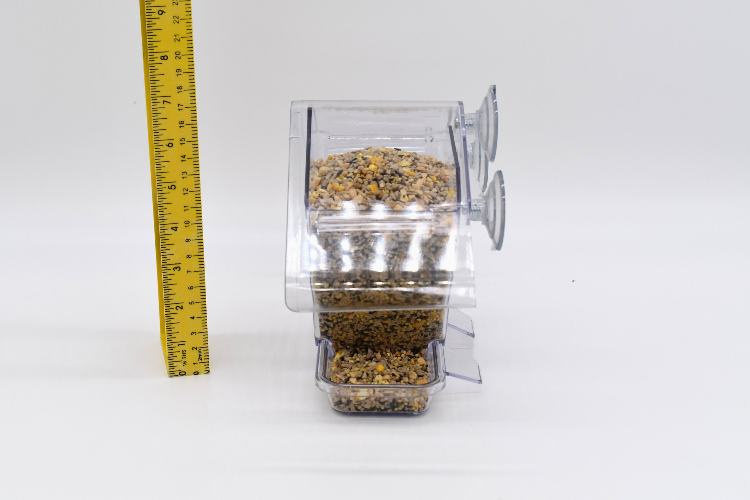 Side profile of the Aspects Window Cafe showing its polycarbonate seed reservoir, feeding tray, and suction cup window mounting system beside a measuring ruler.