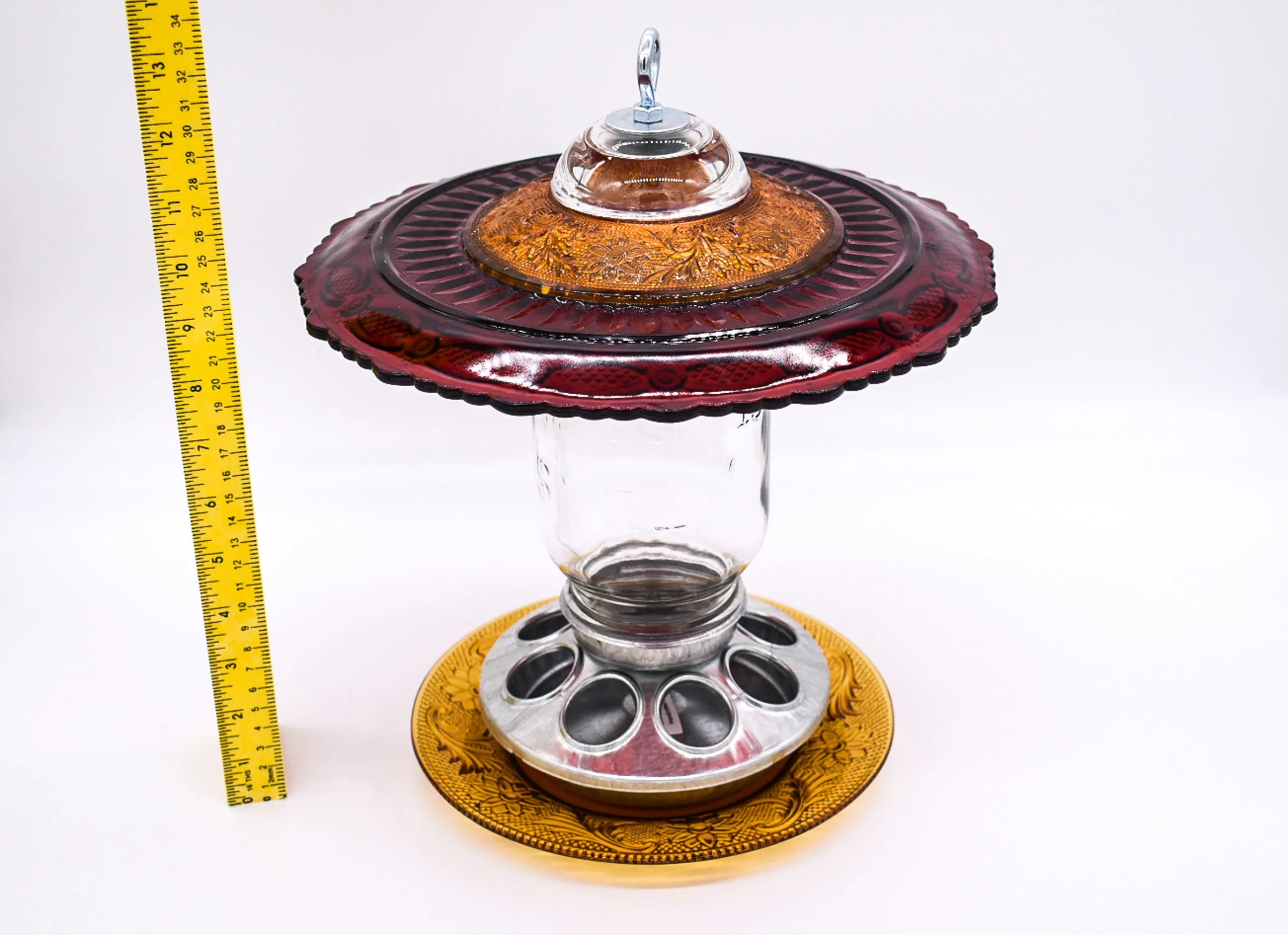 Elevated view of ruby red Avon Cape Cod glass bird feeder showing the decorative amber glass top, Mason jar, and metal seed feeding ports.